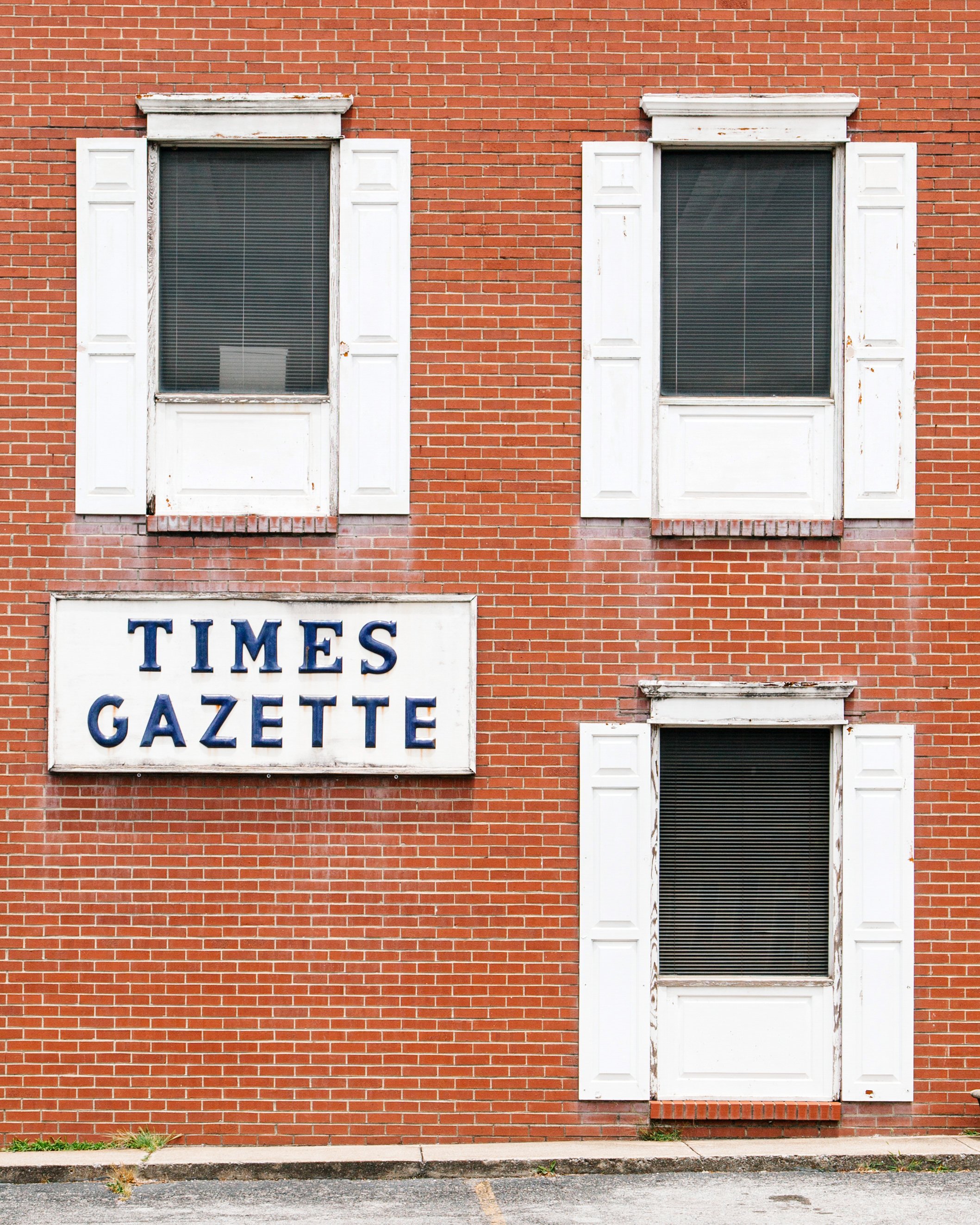 Brick building with three windows, white shutters, and a sign that reads "TIMES GAZETTE".