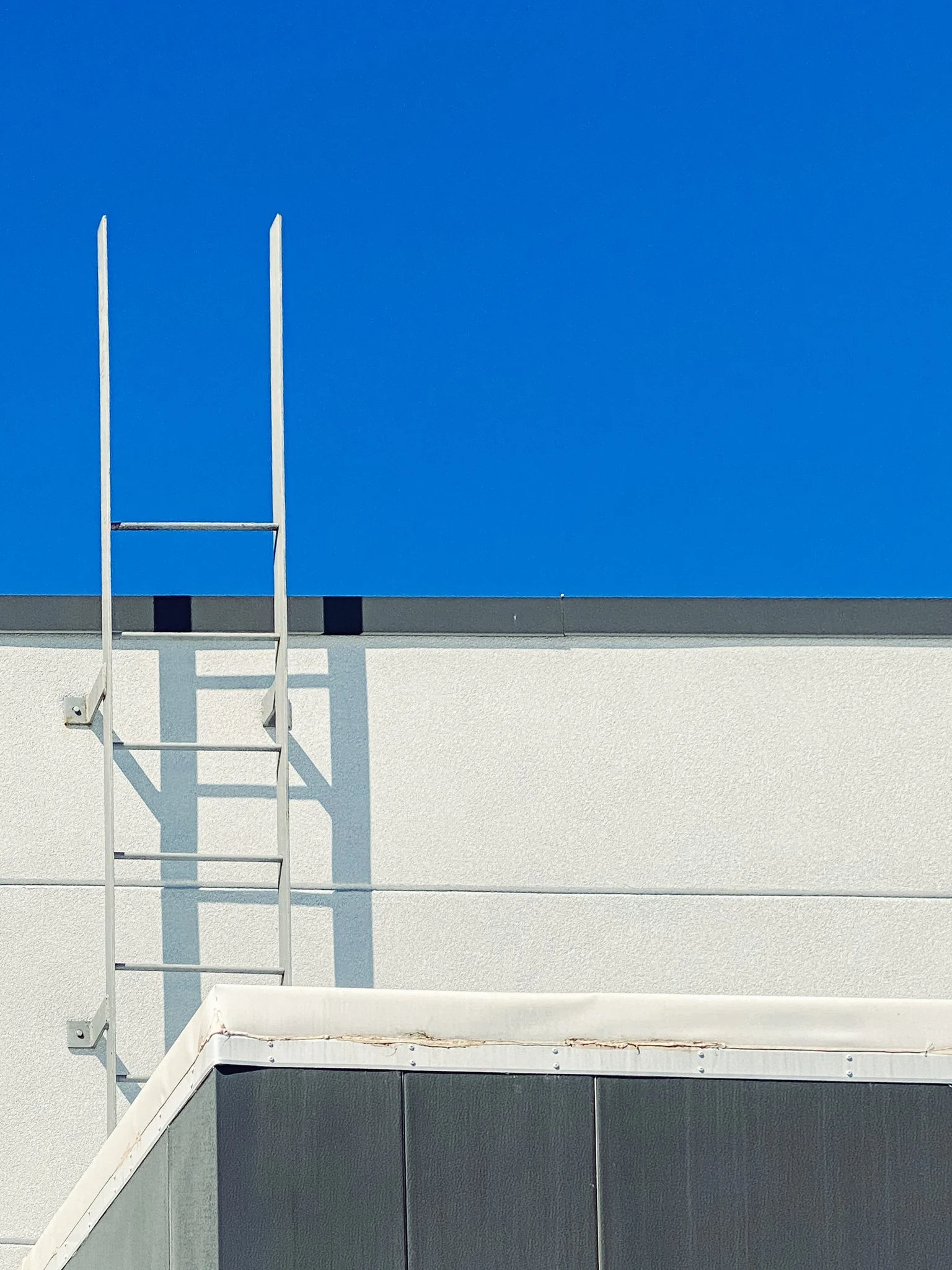 Modern building exterior with white ladder on beige wall, blue sky background.