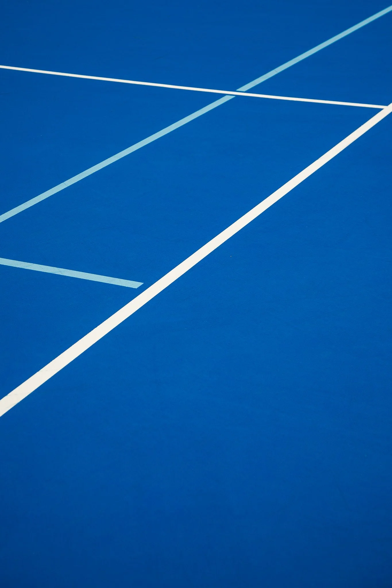 Close-up view of a bright blue tennis or basketball court with white boundary lines.