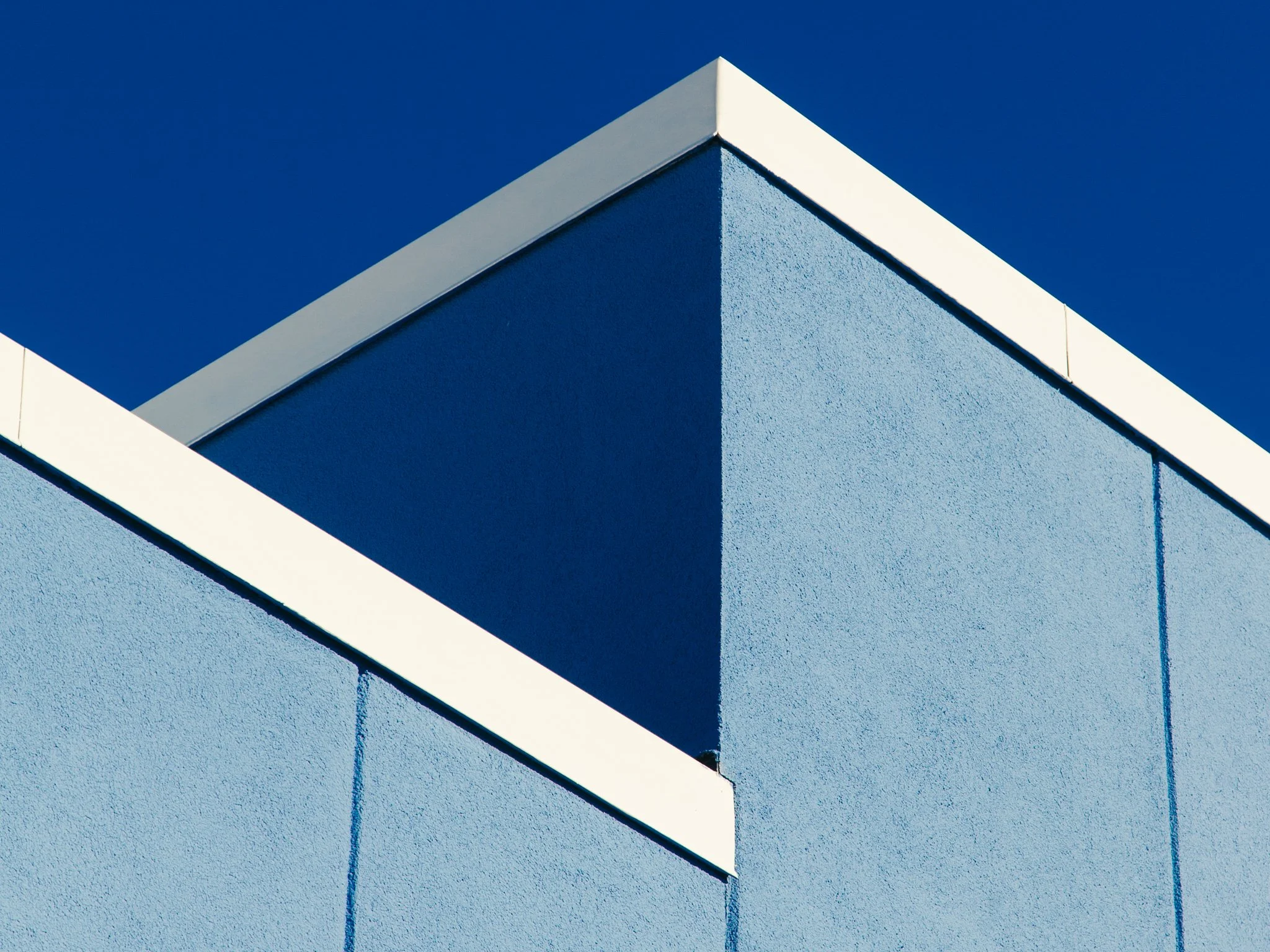 Close-up of a corner of a modern building with a blue exterior wall and white trim against a clear blue sky.