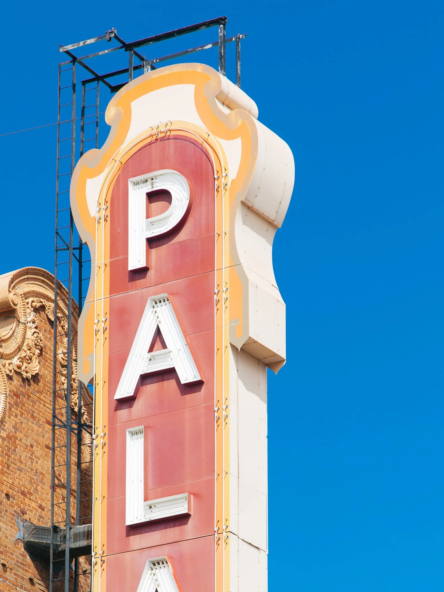 A vintage-style neon sign for a theater or cinema, with the letter 'P' partially visible, mounted on a colorful building against a clear blue sky.