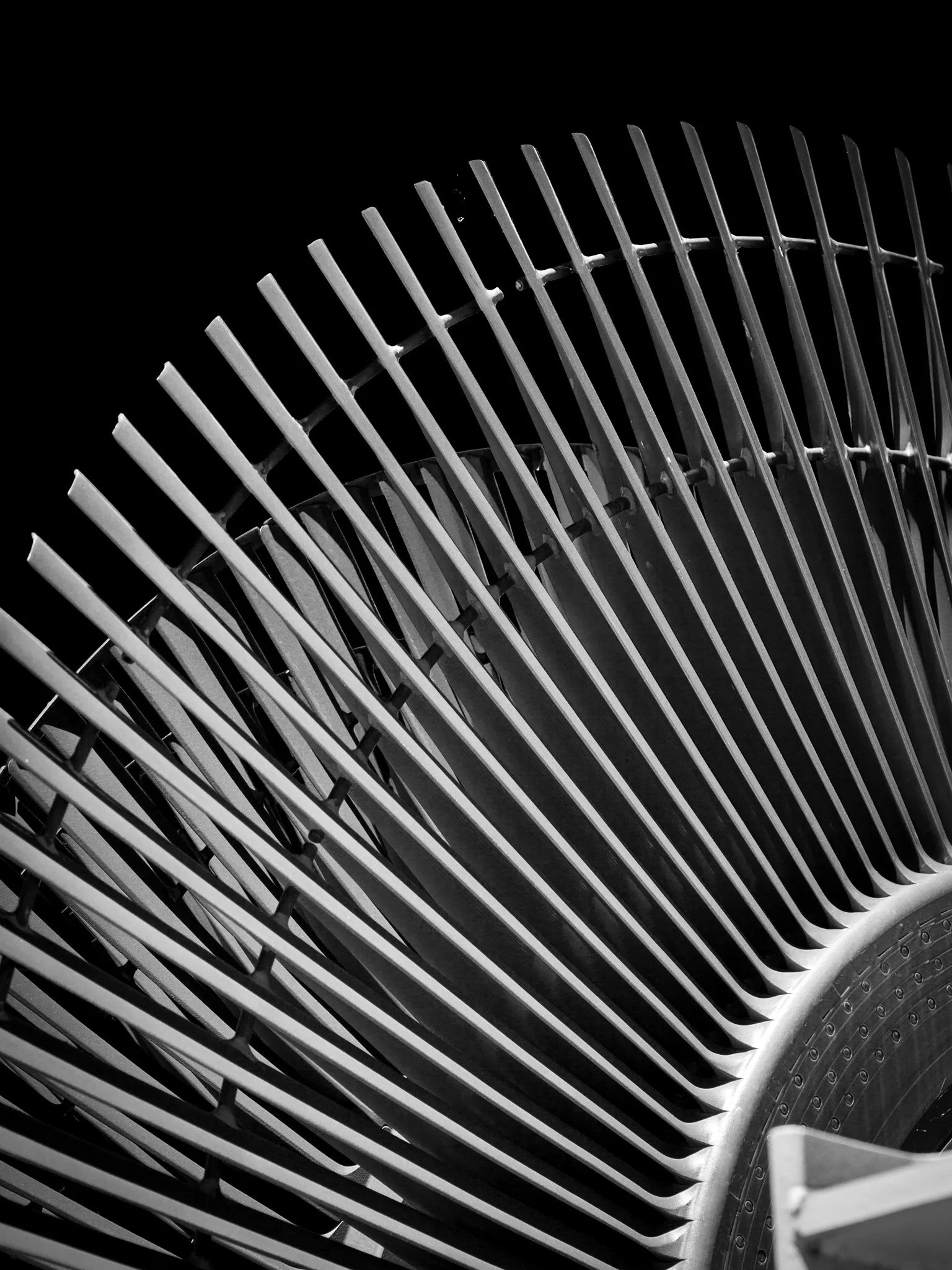 Close-up of metal chair or bench with slats in black and white, showing a curved design and mesh-backed seating area.
