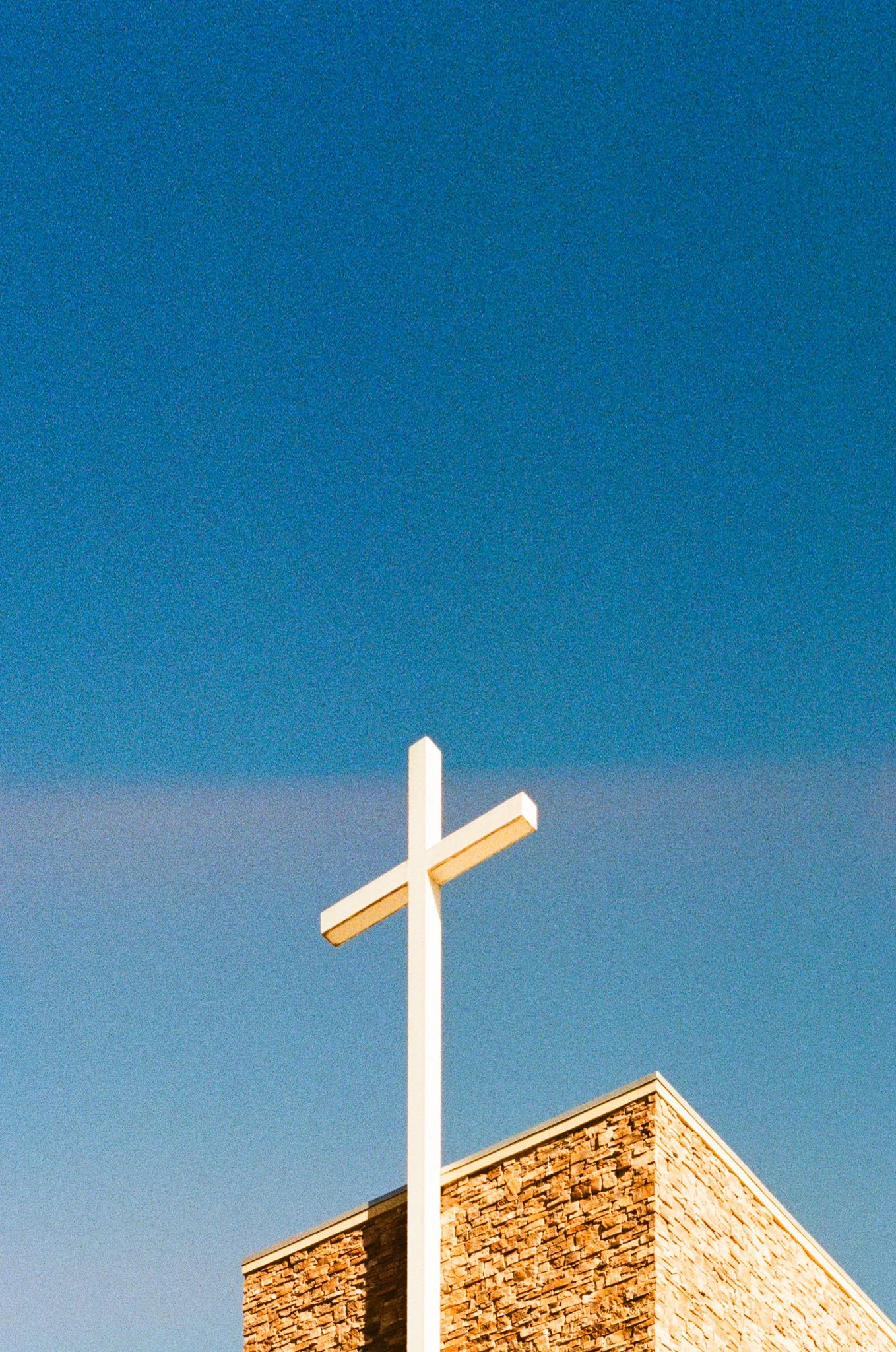 Christian cross atop a stone church building against a clear blue sky.