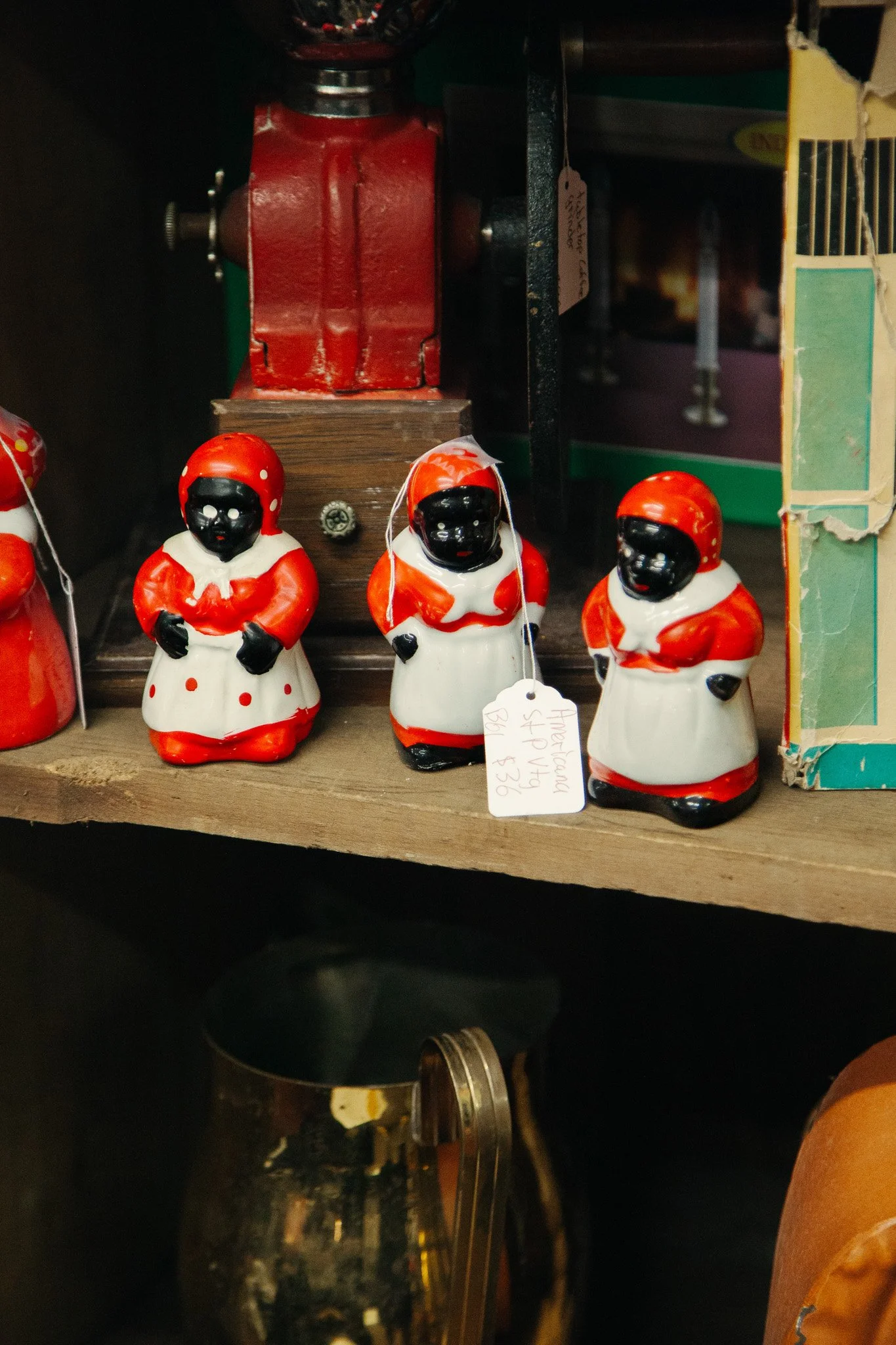 A display of vintage figurines of black-faced children dressed as Santa Claus, with red and white outfits, in front of a red-painted vice clamp on a shelf.