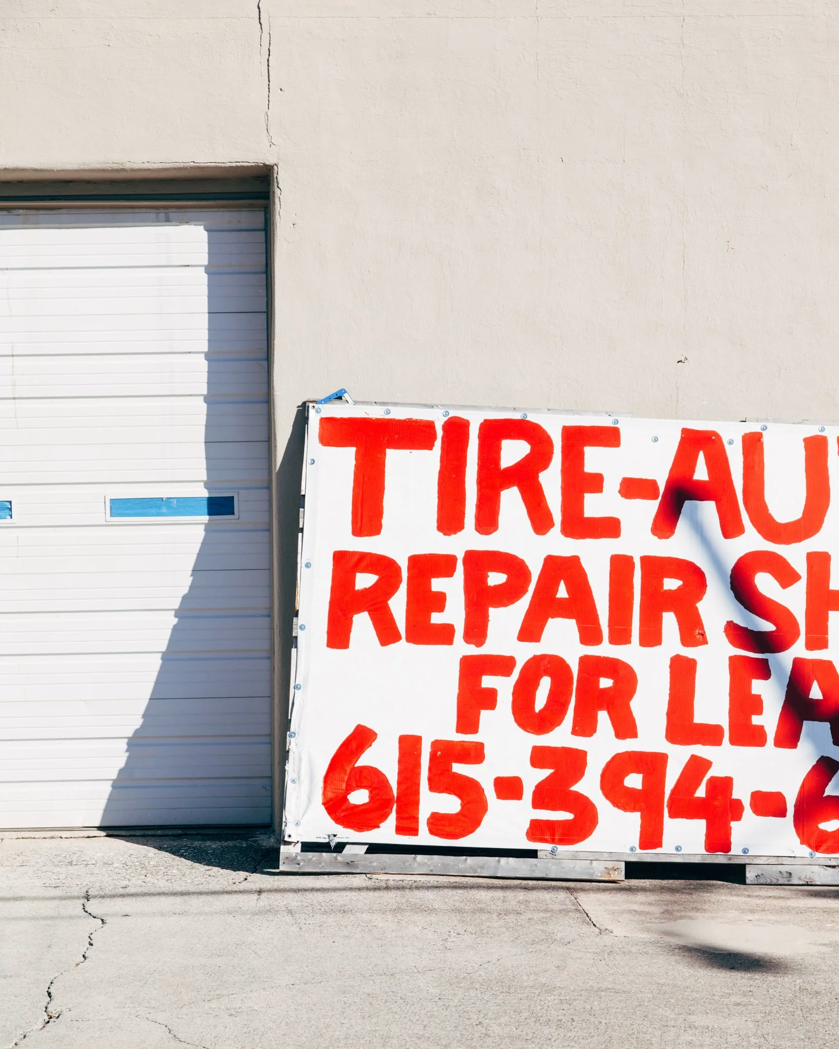 White building with a closed garage door and a sign with red text saying "TIRE-" and more words partially visible.