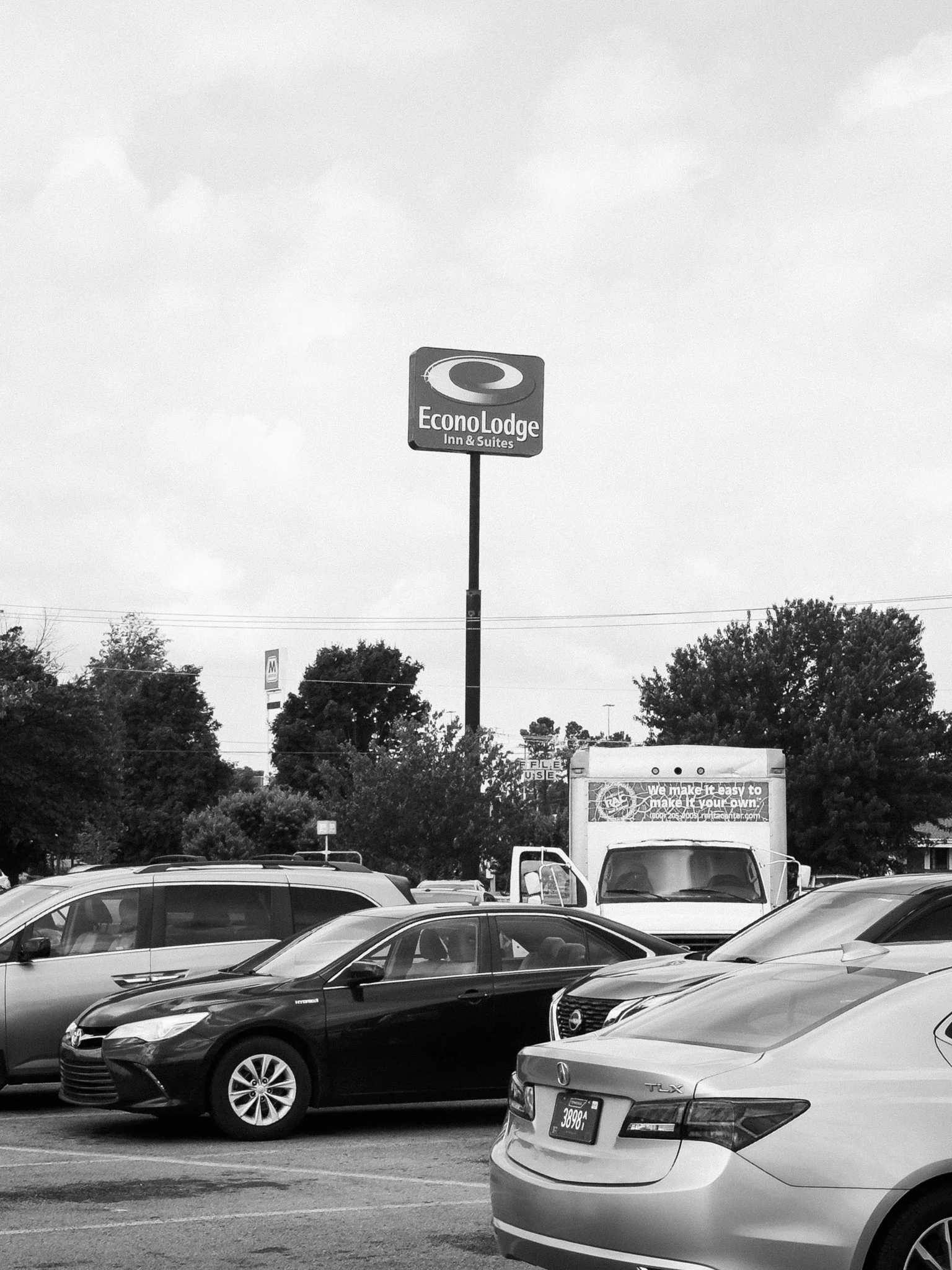 A parking lot filled with various cars and trucks, with an EconoLodge motel sign and some trees in the background.