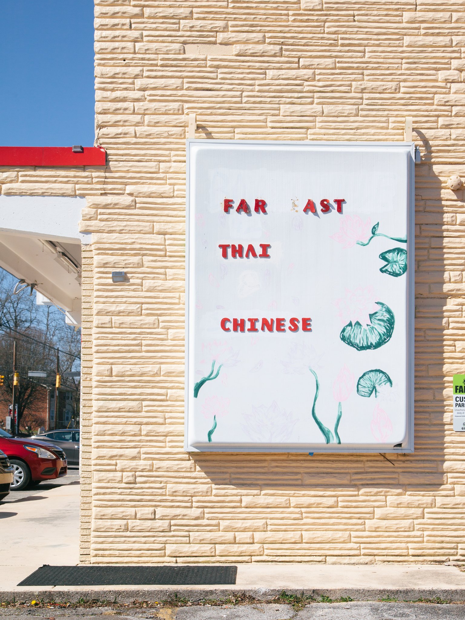 Whiteboard on a beige brick wall with painted floral designs and red letters spelling 'FAR EAST CHINESE'.
