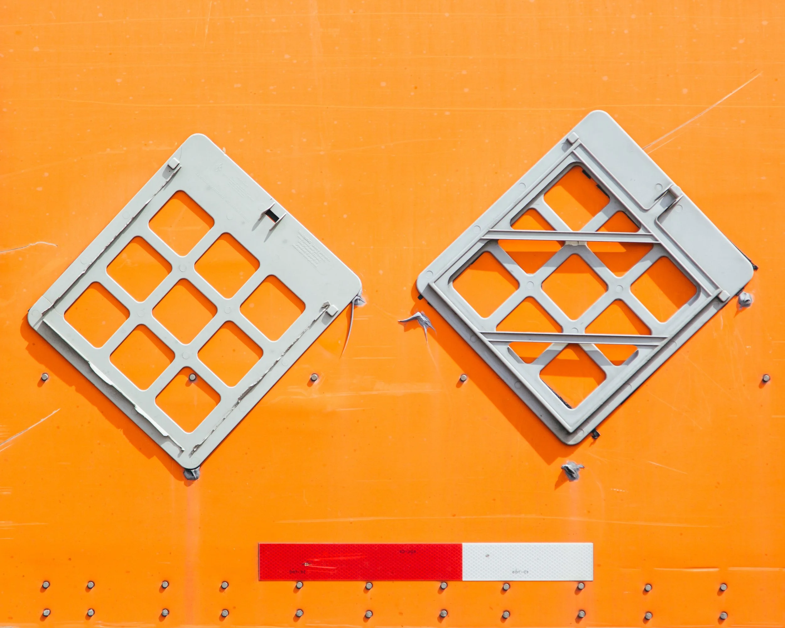 Two gray plastic crate-like objects with grid patterns sit on an orange surface, with a red and white rectangular label below them.