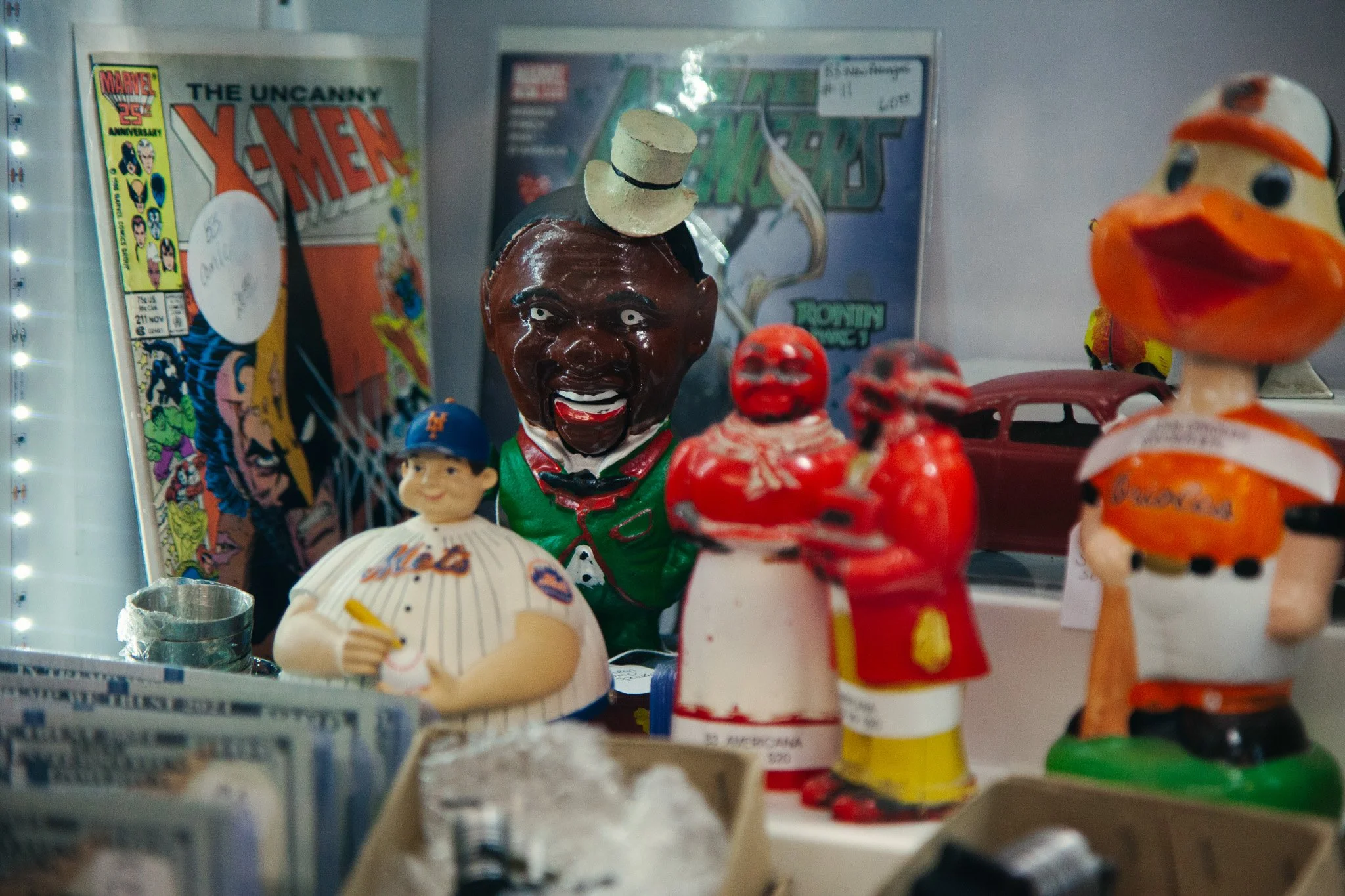 Display of vintage collectibles including a ceramic figure of a chef, a plush toy of a duck, and a comic book, along with some cash, inside a glass cabinet.