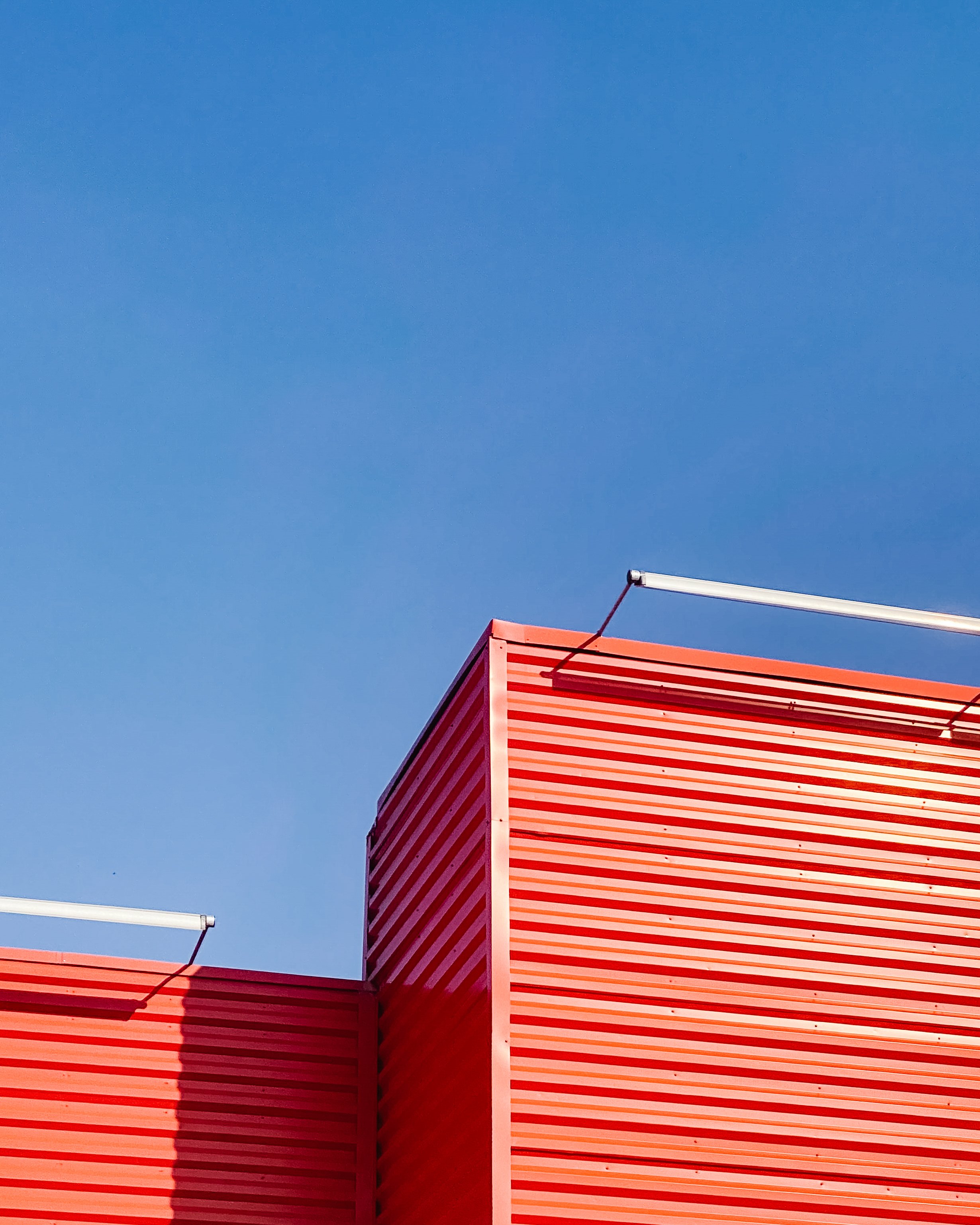 Part of a modern red building with horizontal siding and a white-framed opening, against a clear blue sky.