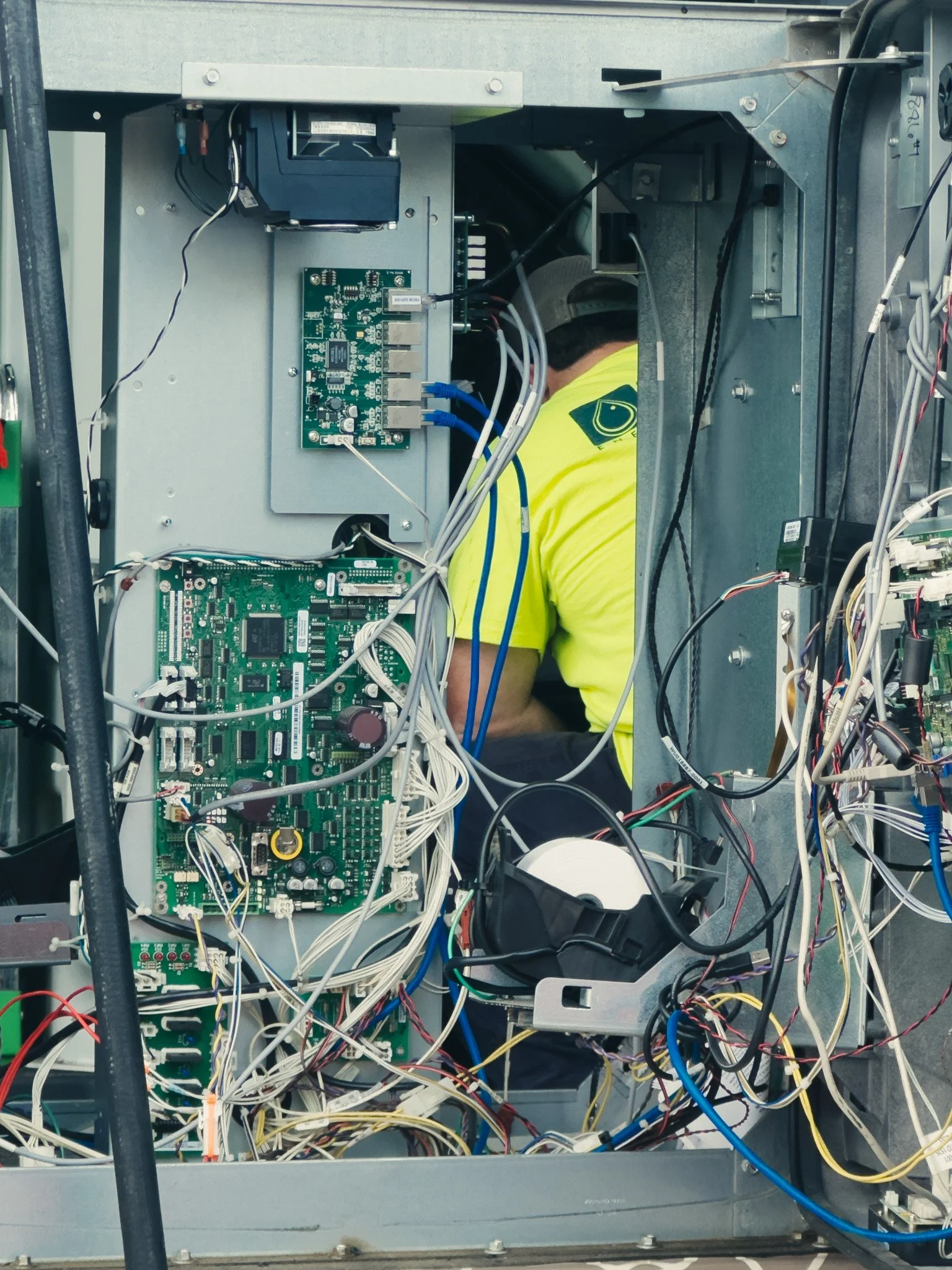A technician working inside an open electronic control panel with various circuit boards, wires, and components.