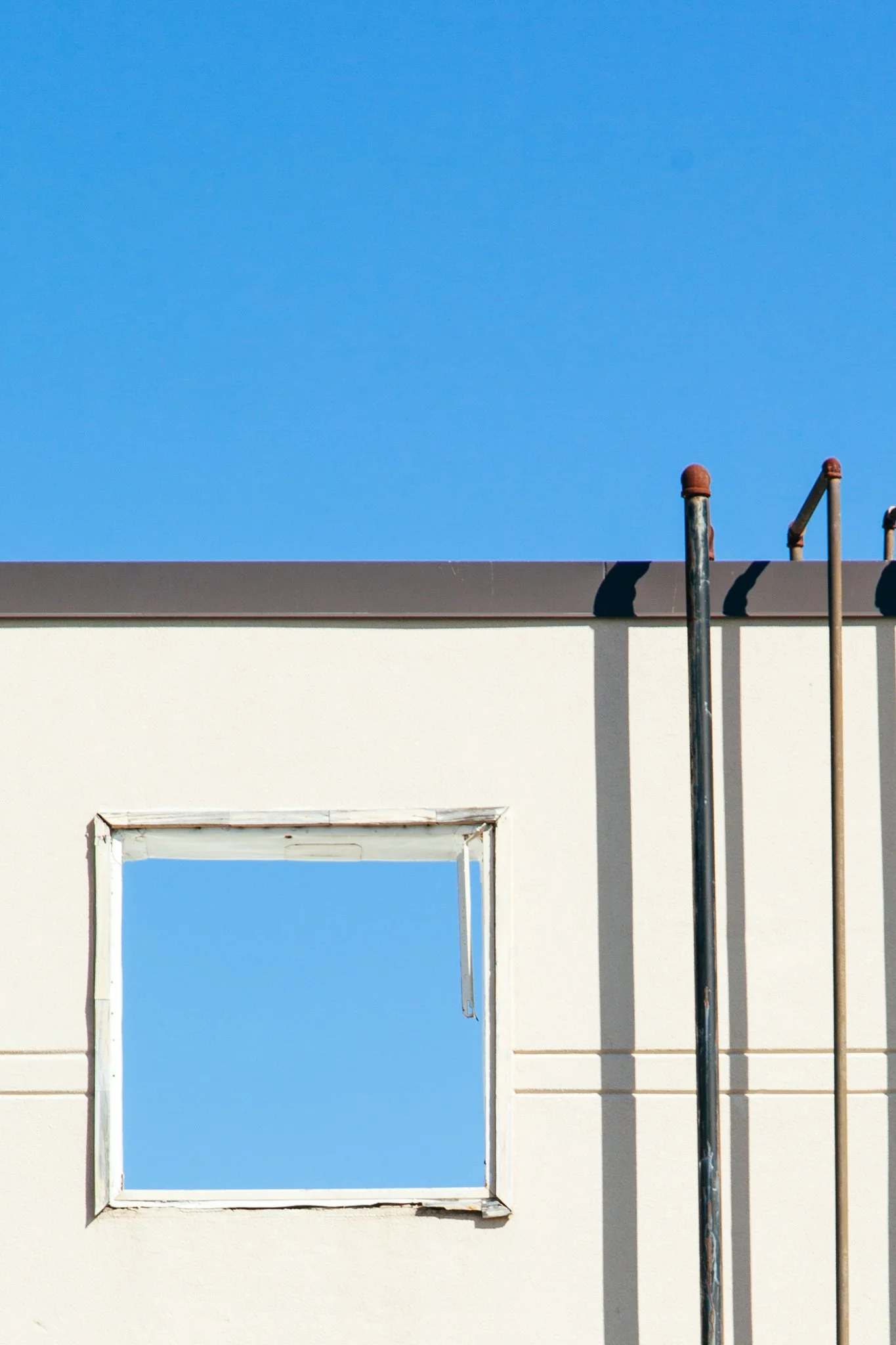 Part of a building's wall with a window opening, blue sky visible through the opening, and construction or utility pipes on the right side.