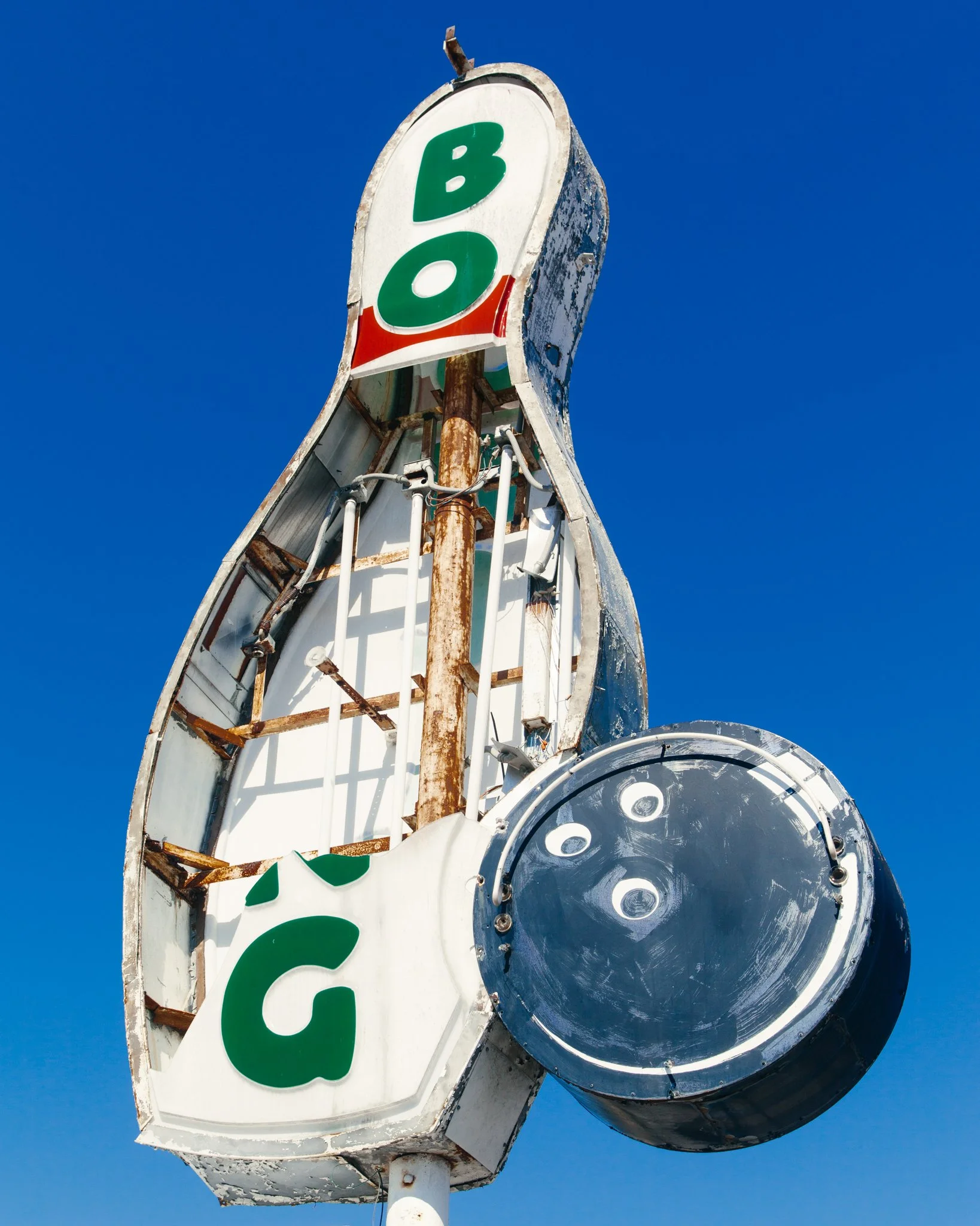 Old, weathered sign for a bingo hall with missing text, showing rust and peeling paint, under a clear blue sky.