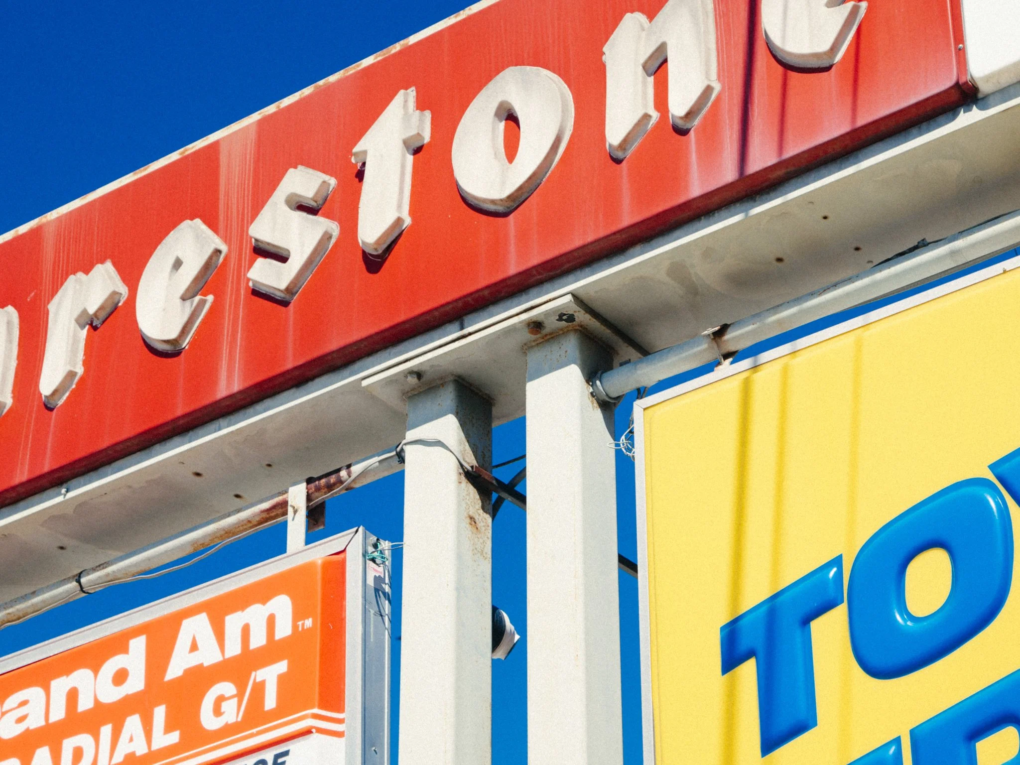 Close-up of a colorful sign with the words 'Elec Toy' and part of an orange sign reading 'and A'I', with a clear blue sky in the background.