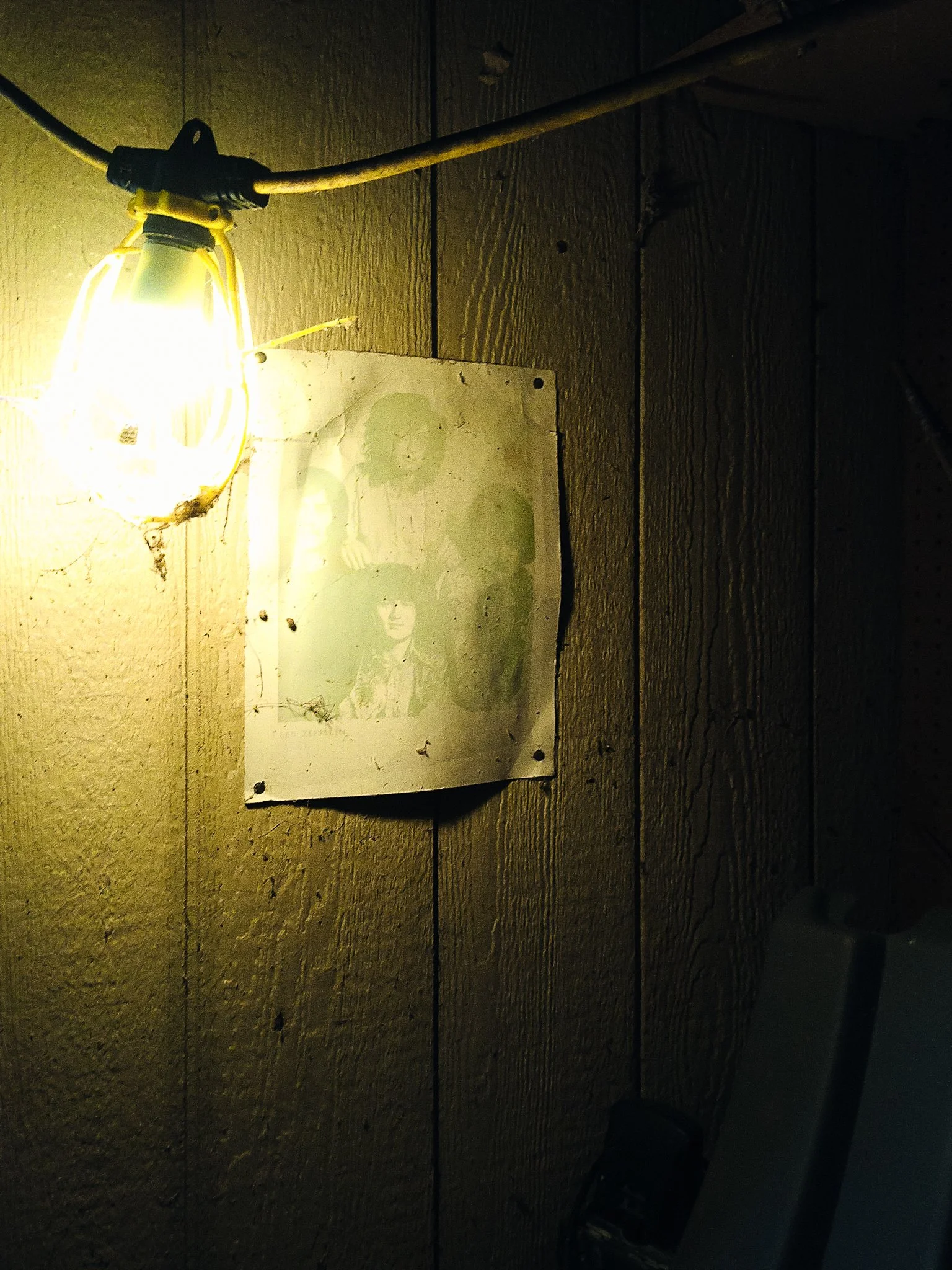 Dimly lit wooden wall with a yellow light bulb and a weathered poster of women in glasses.