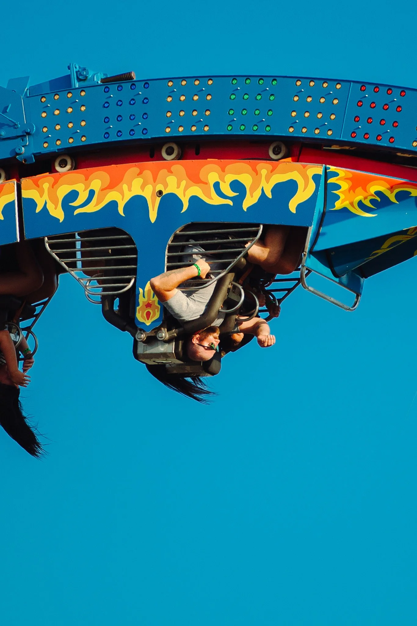 People riding a colorful amusement park ride against a clear blue sky.