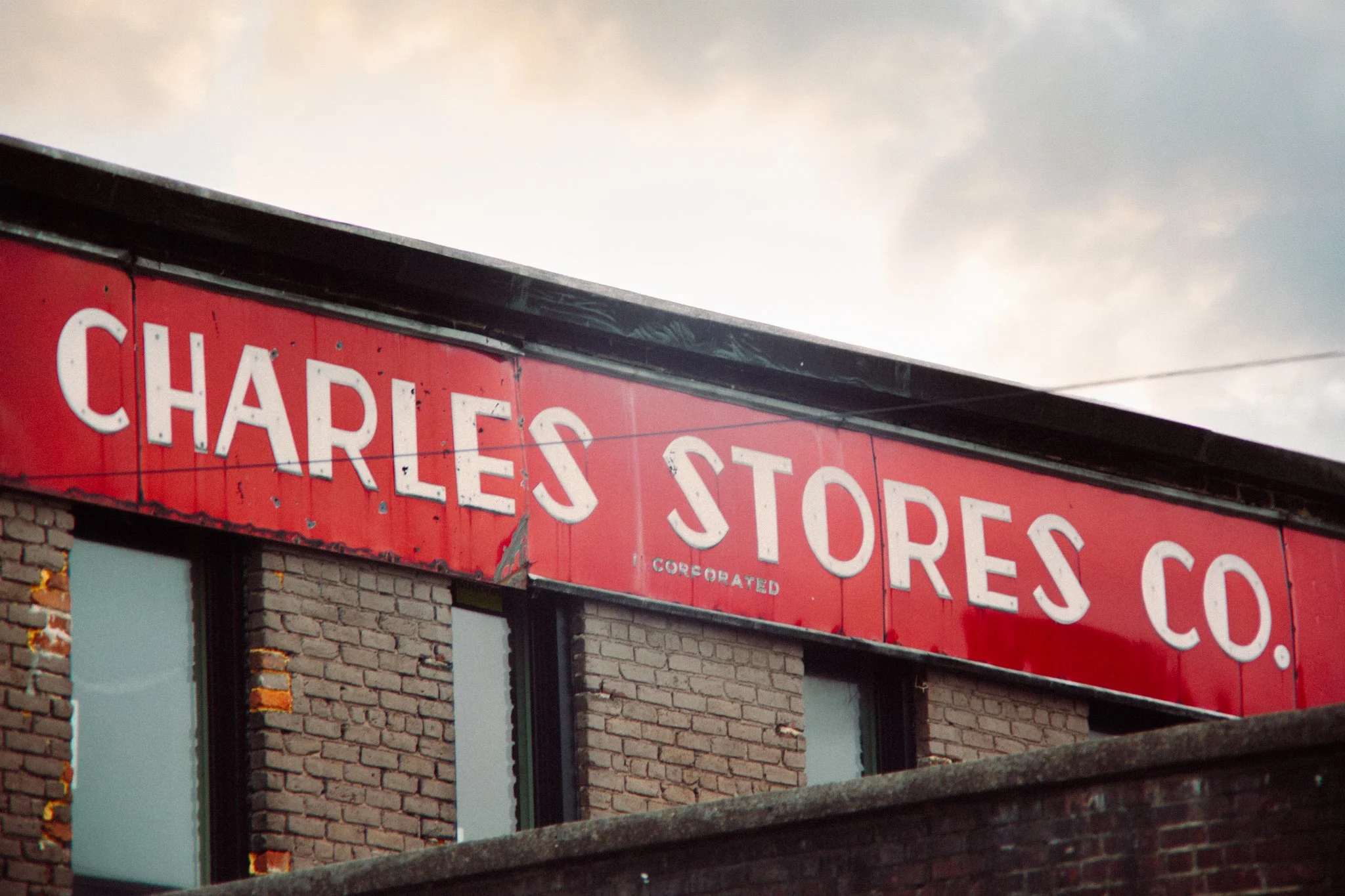Close-up of a red sign with the words 'Charles Store' on a brick building, under a cloudy sky.