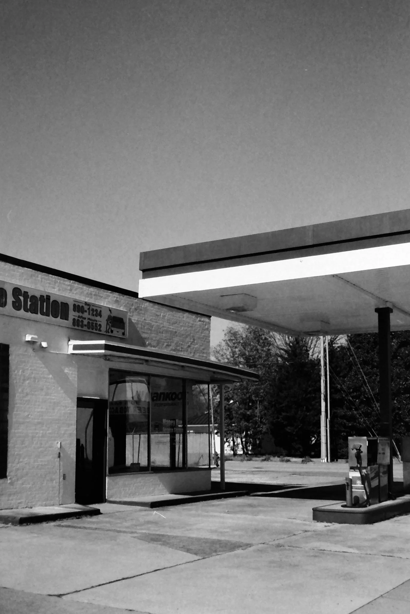 Black and white photo of a fast food restaurant with a large canopy over the drive-thru window and a sign in the background.
