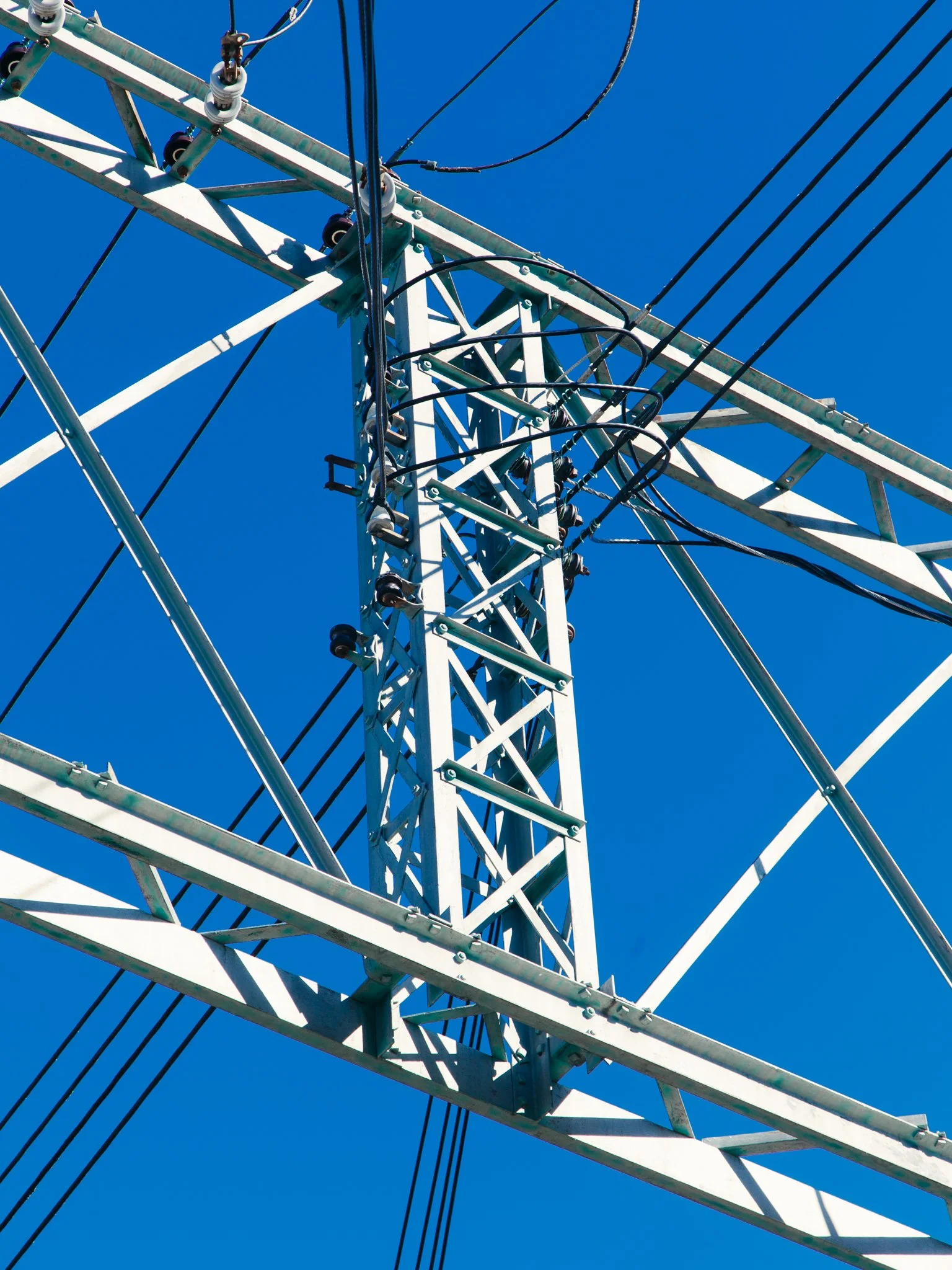 Close-up view of a tall electrical transmission tower made of metal with wires and insulators against a clear blue sky.