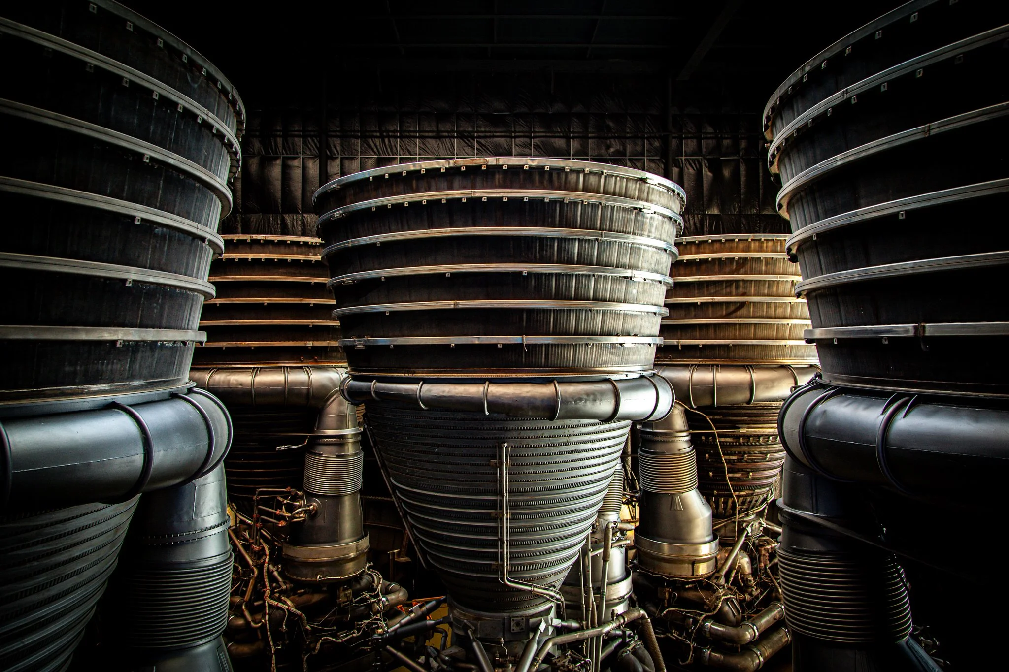 Large industrial turbines with metallic surfaces and complex piping system in a dark, industrial setting.
