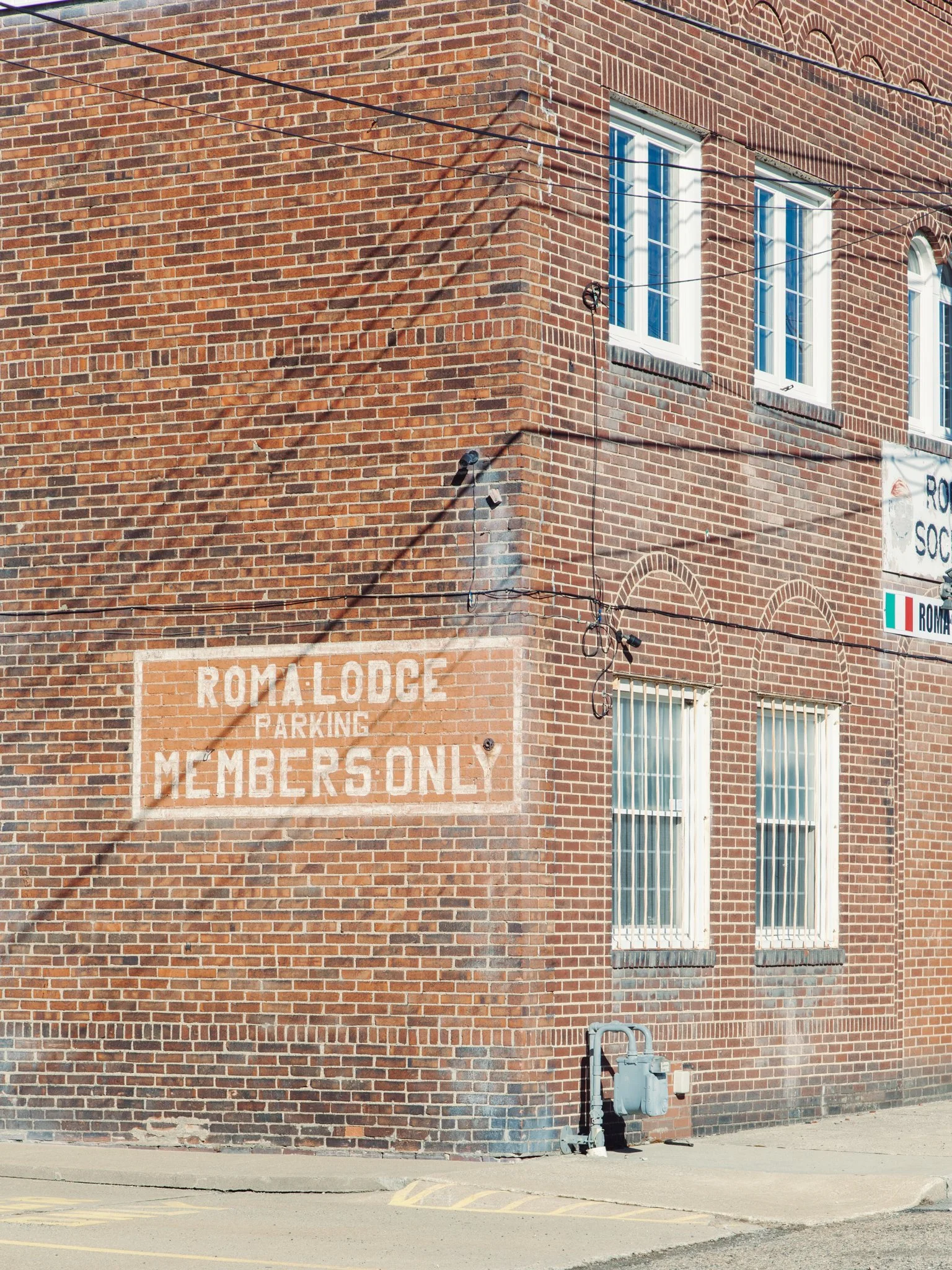 Brick building with multiple windows and a faded sign that reads 'ROMA LODGE PARKING MEMBERS ONLY'.