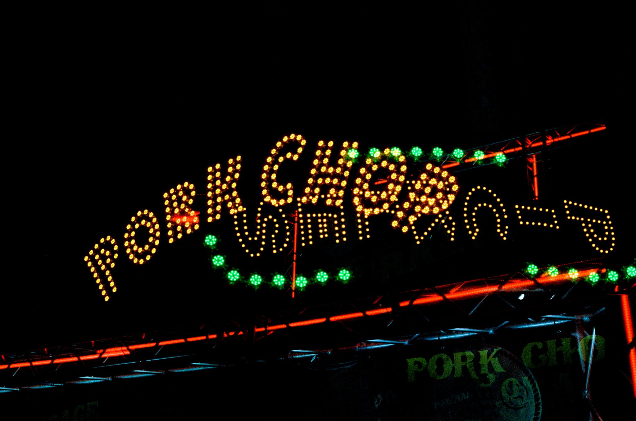 Brightly lit sign at night with yellow and green lights forming the words 'Krazy'.
