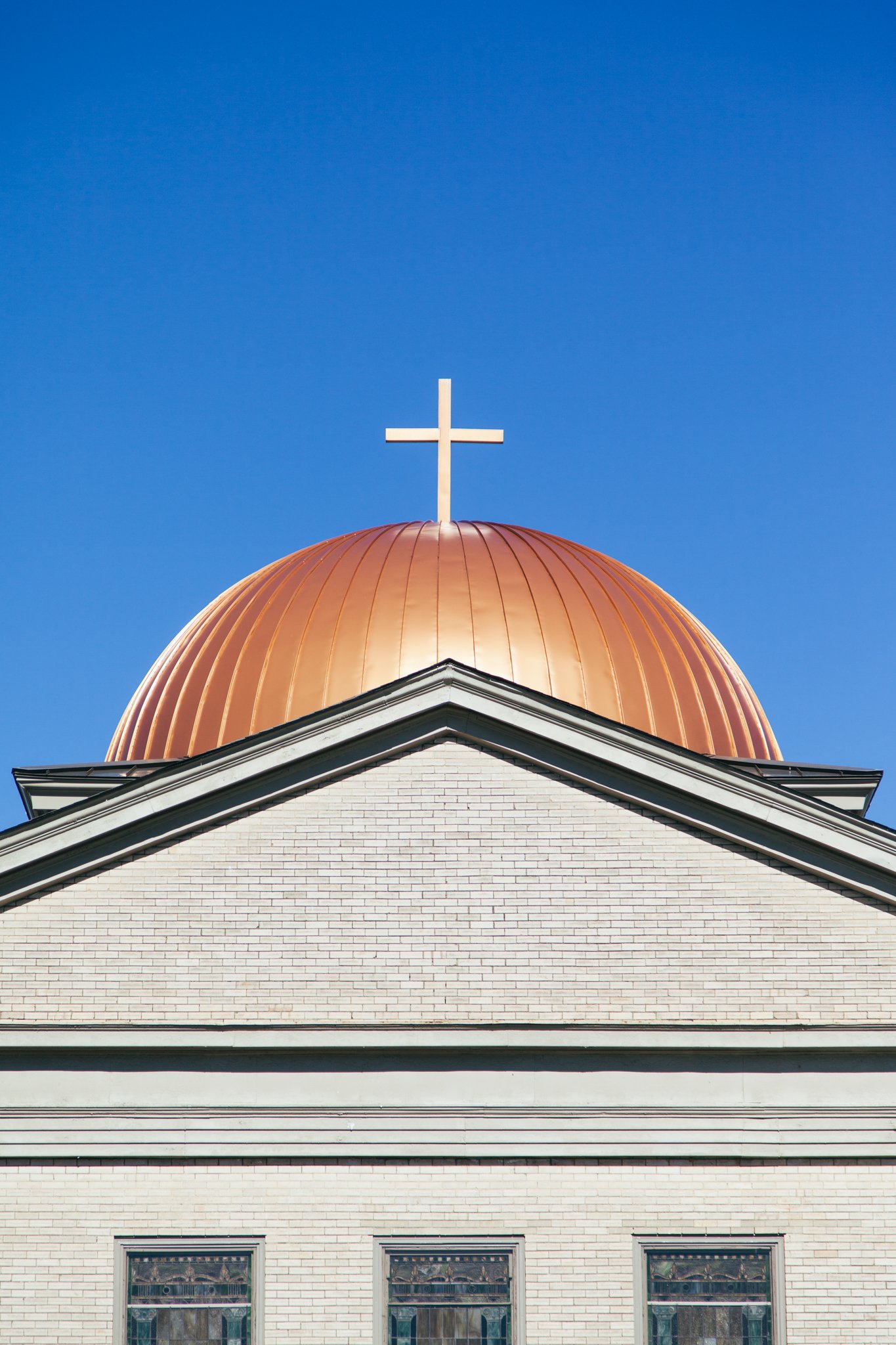 The top of a white brick church building with a golden dome roof and a white cross on top, set against a clear blue sky.