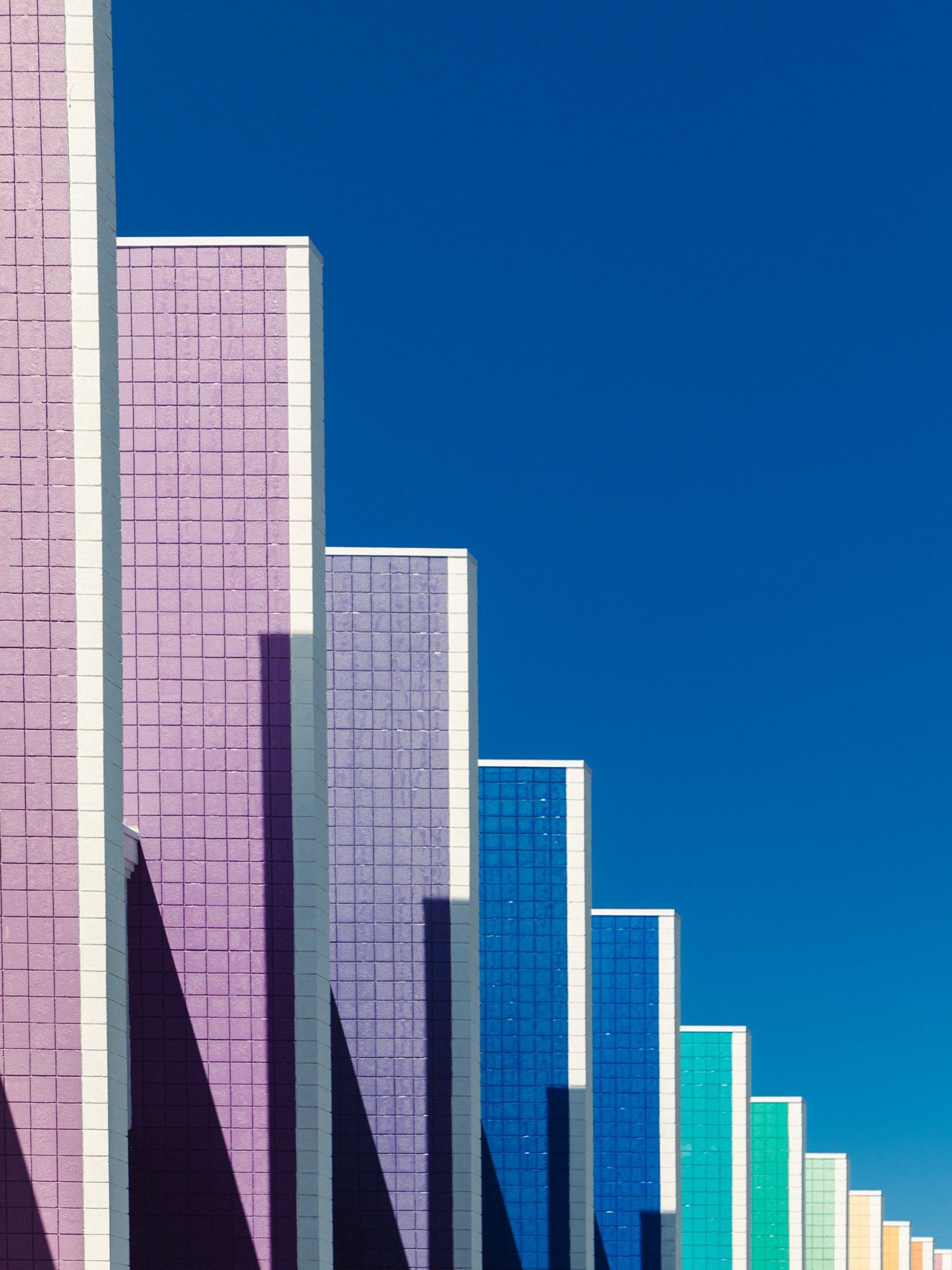Colorful skyscraper with a pink, purple, blue, and yellow gradient pattern on the exterior, set against a clear blue sky.