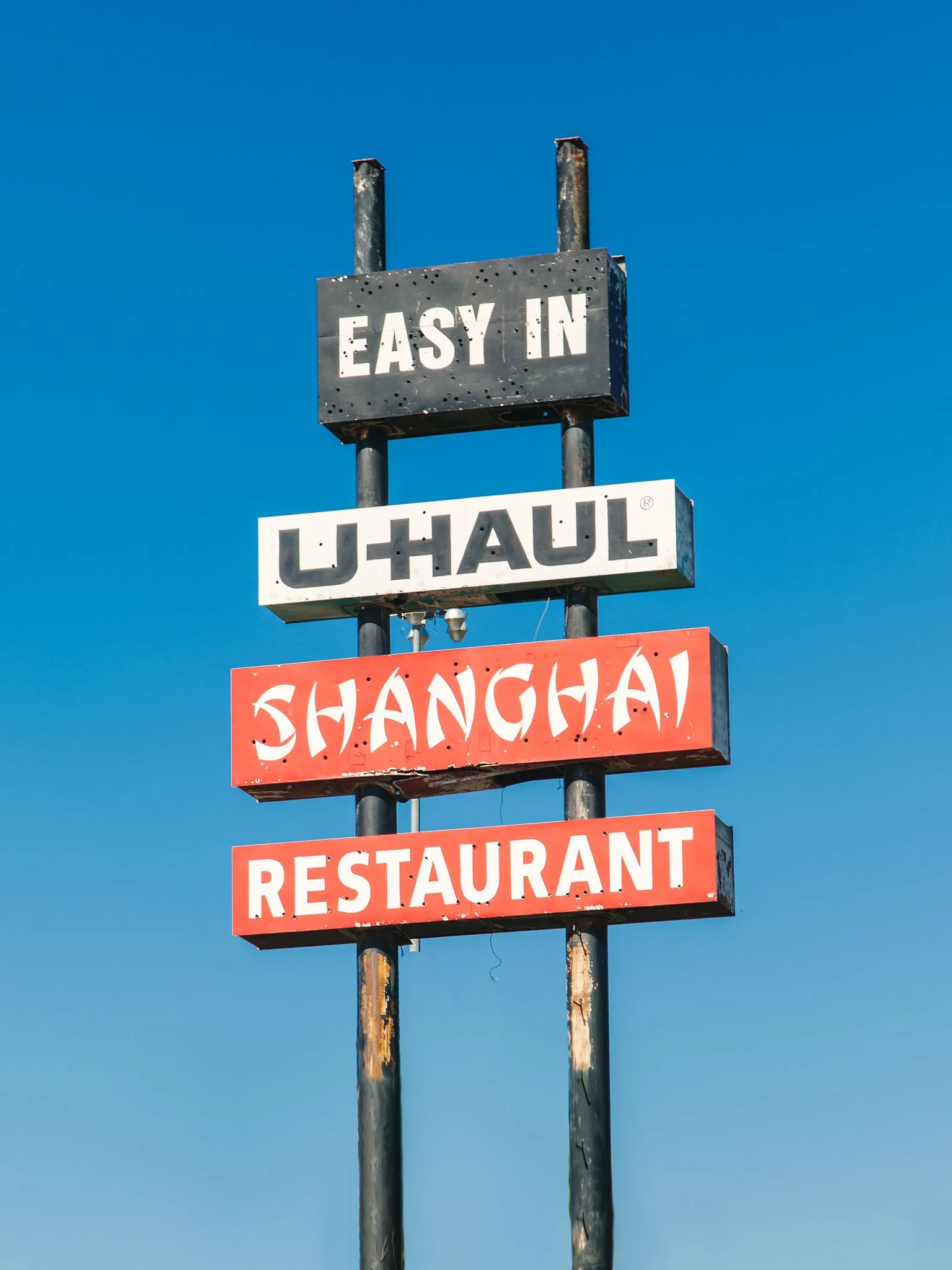 A multi-tiered signpost featuring signs for 'Easy In,' 'U-Haul,' 'Chinatown,' and 'Restaurant' against a clear blue sky.