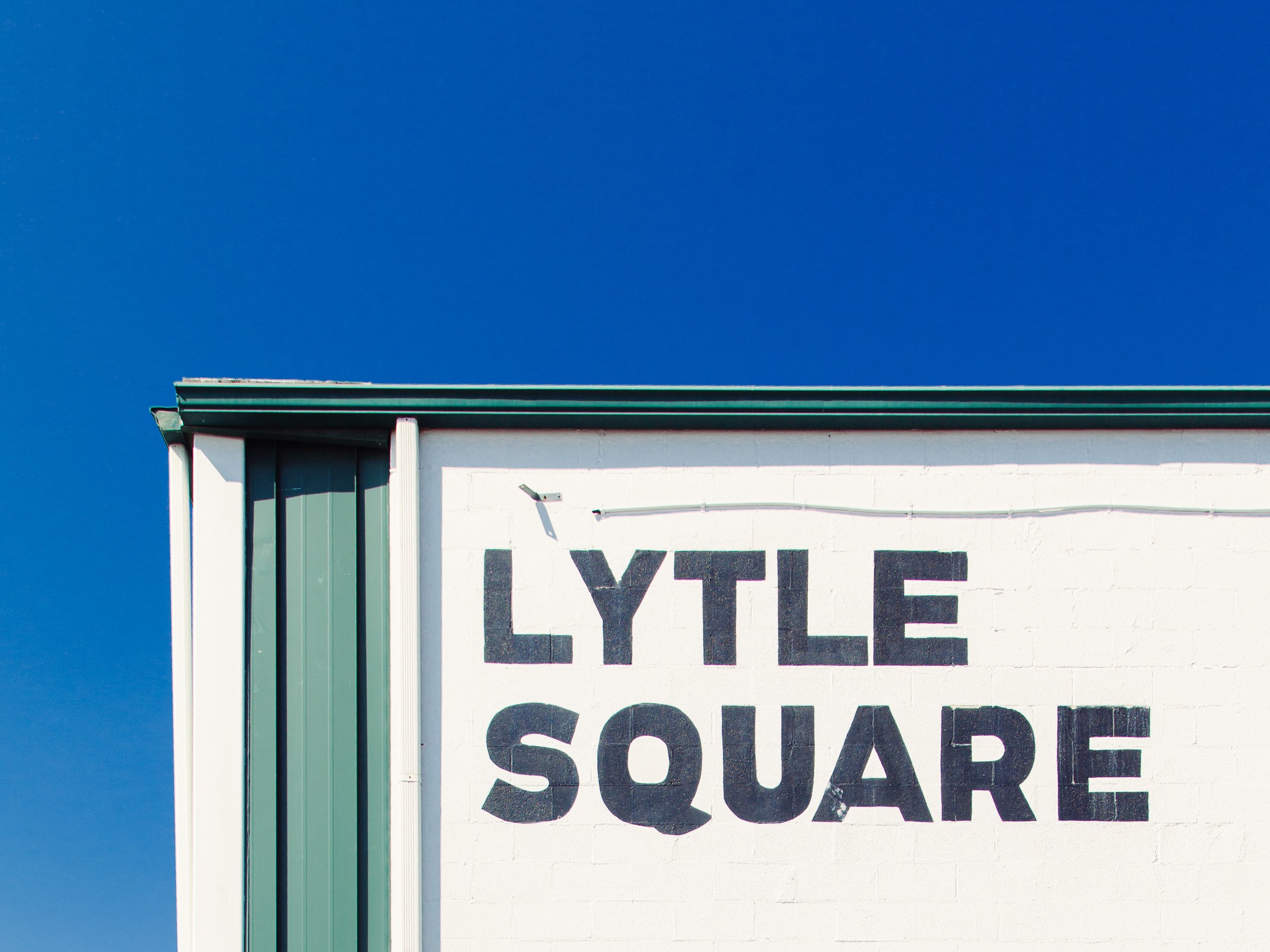 Part of a building corner with a white wall that has black text, a green corner trim, and a clear blue sky in the background.