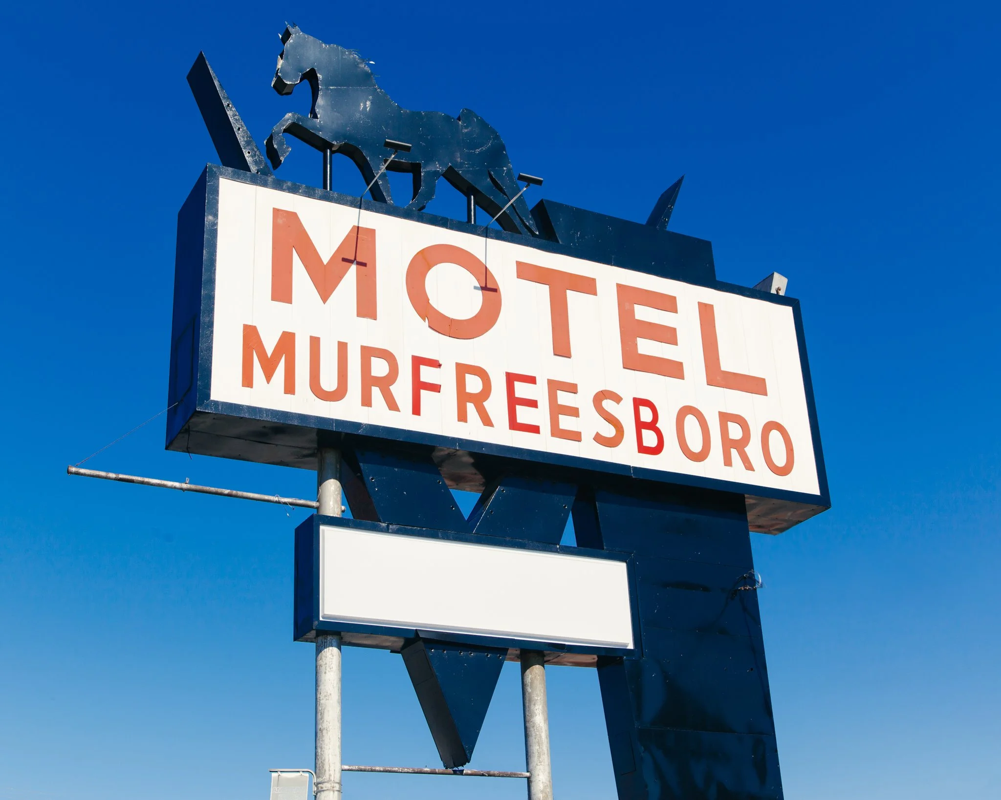 A sign with a black metal horse silhouette and partially visible red text on a white background against a clear blue sky.