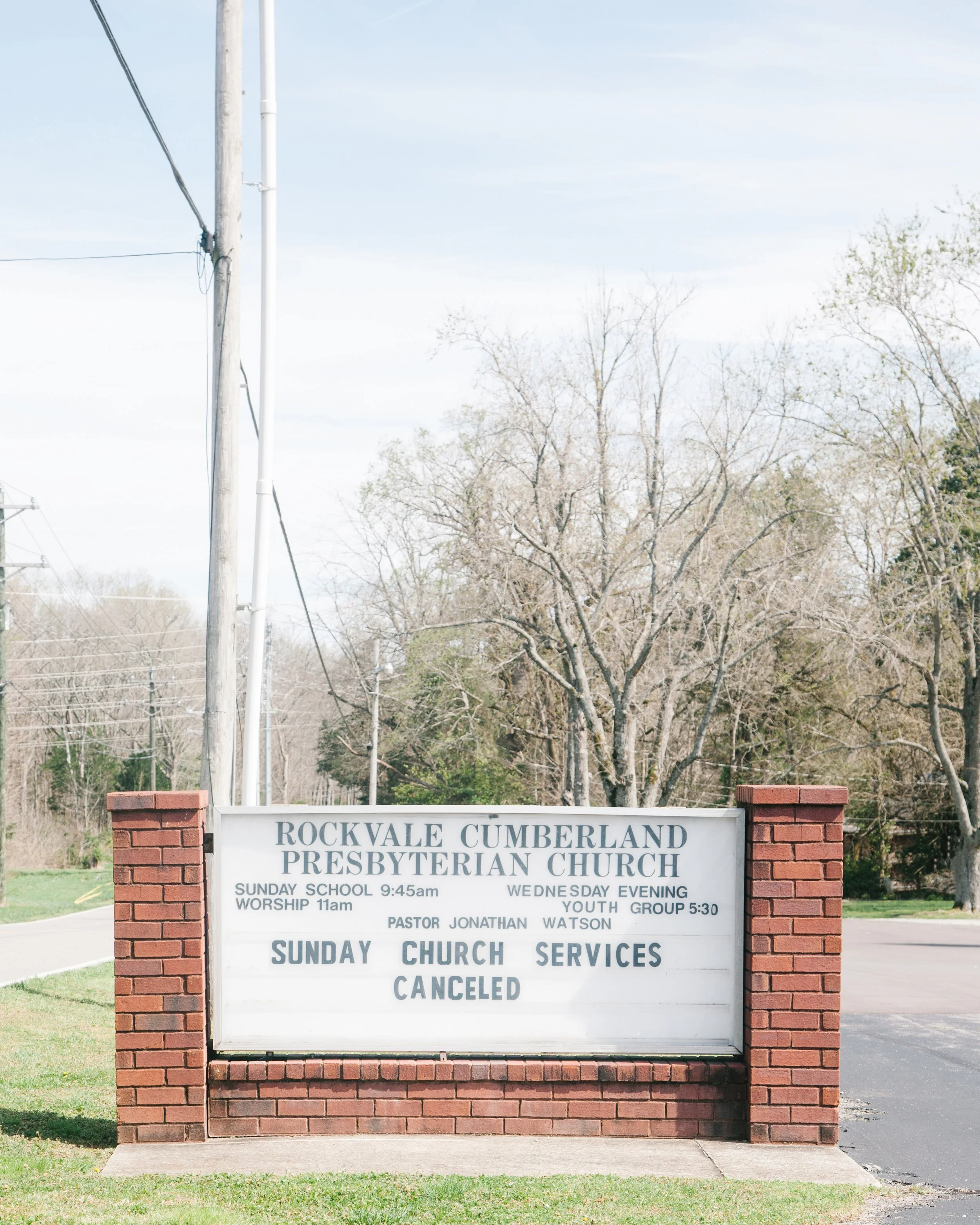 A brick sign in front of trees and a partly cloudy sky lists service times and cancellations for Rockyvale Cumberland Presbyterian Church, including Sunday service at 11 am, Sunday school at 9:45 am, youth group at 5:30 pm, and a note that all servic