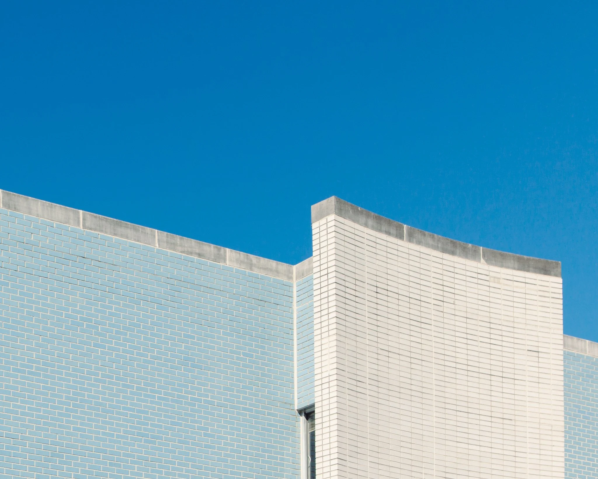 Close-up of a modern building with light blue brick walls and beige accents, set against a clear blue sky.