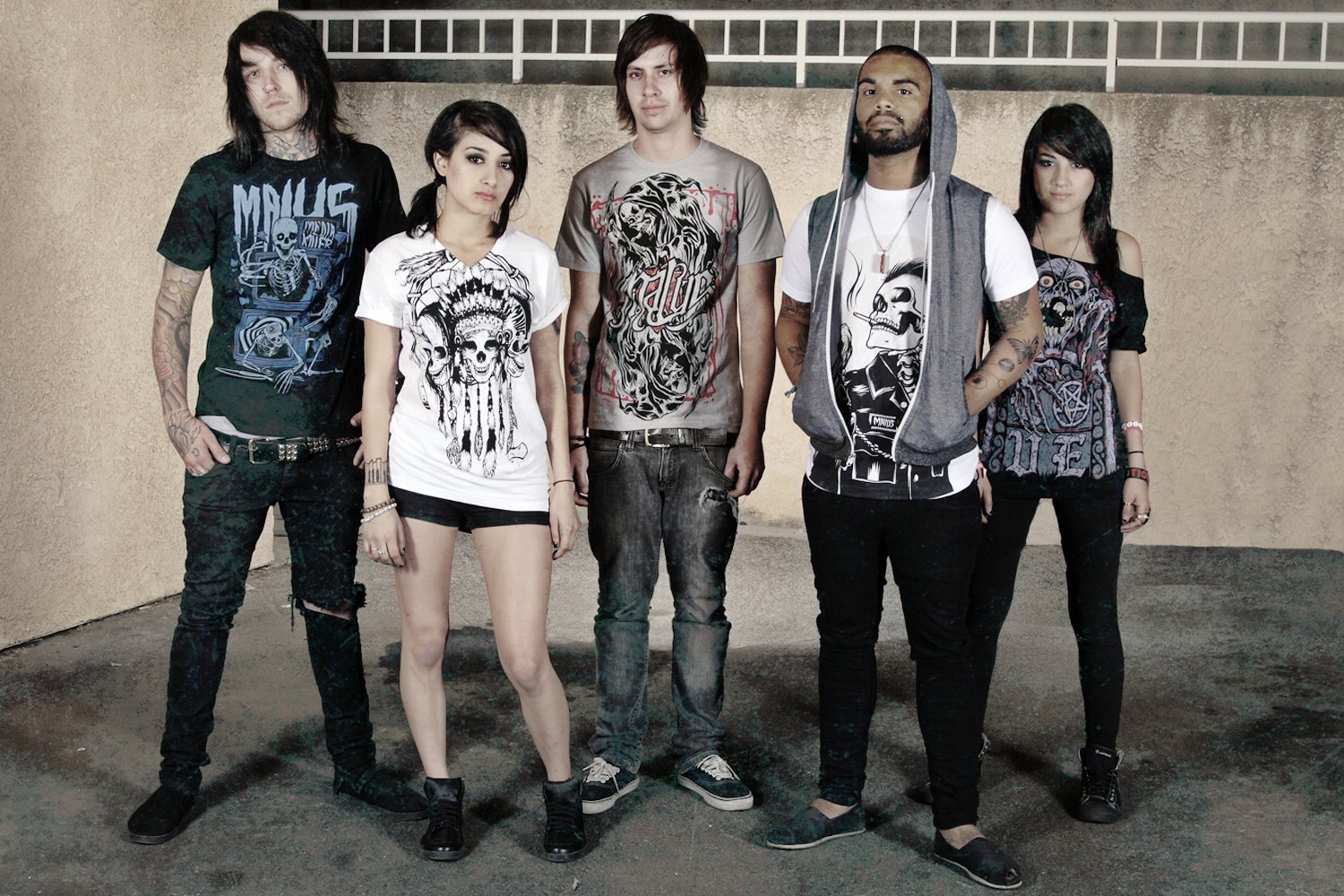 A diverse group of five young adults standing together outdoors against a beige wall, dressed in casual and punk-inspired clothing.