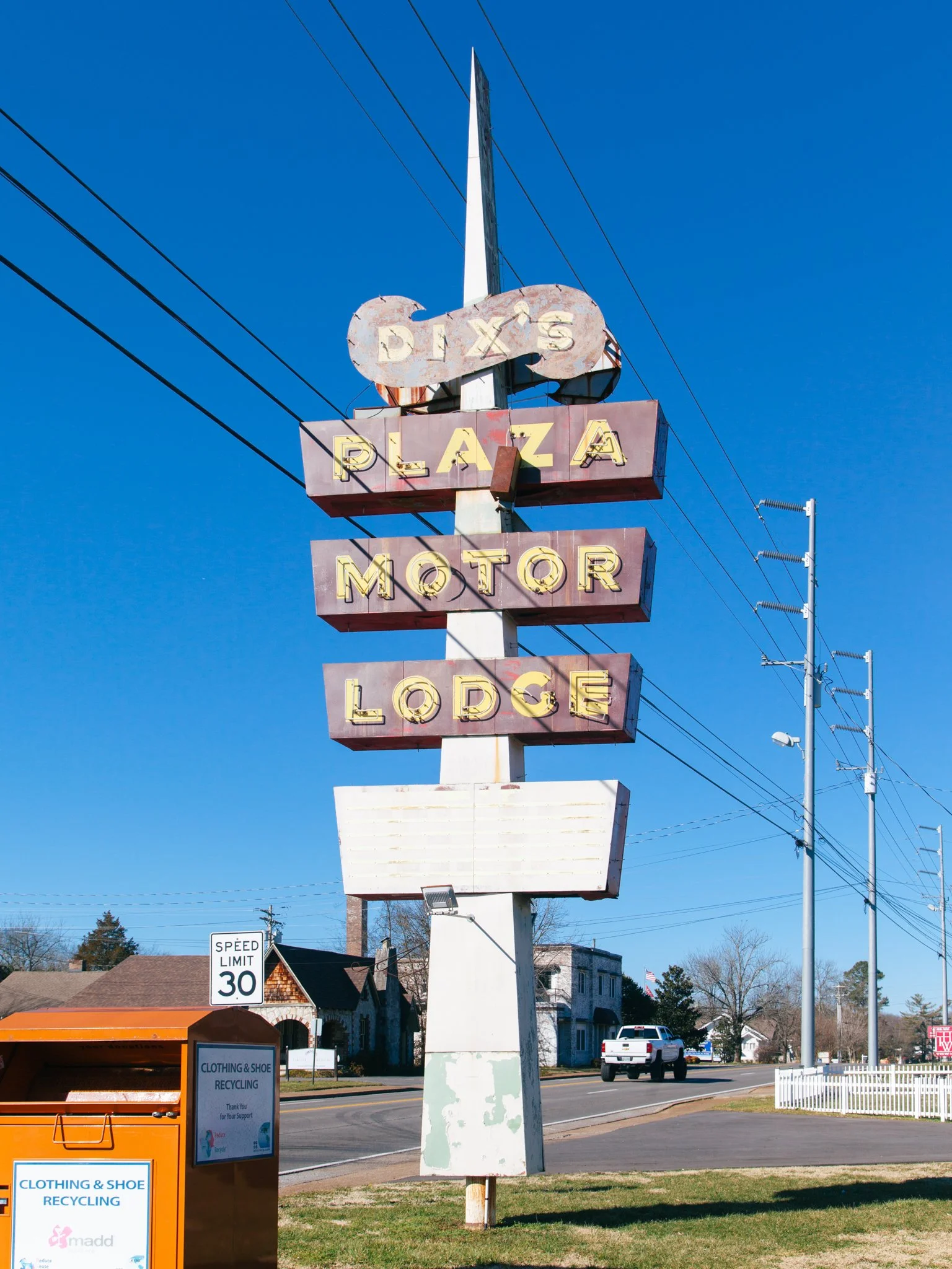 A vintage neon sign reads 'Dix's Plaza Motor Lodge' and is mounted on a tall pole against a clear blue sky. The sign's paint is weathered and faded.
