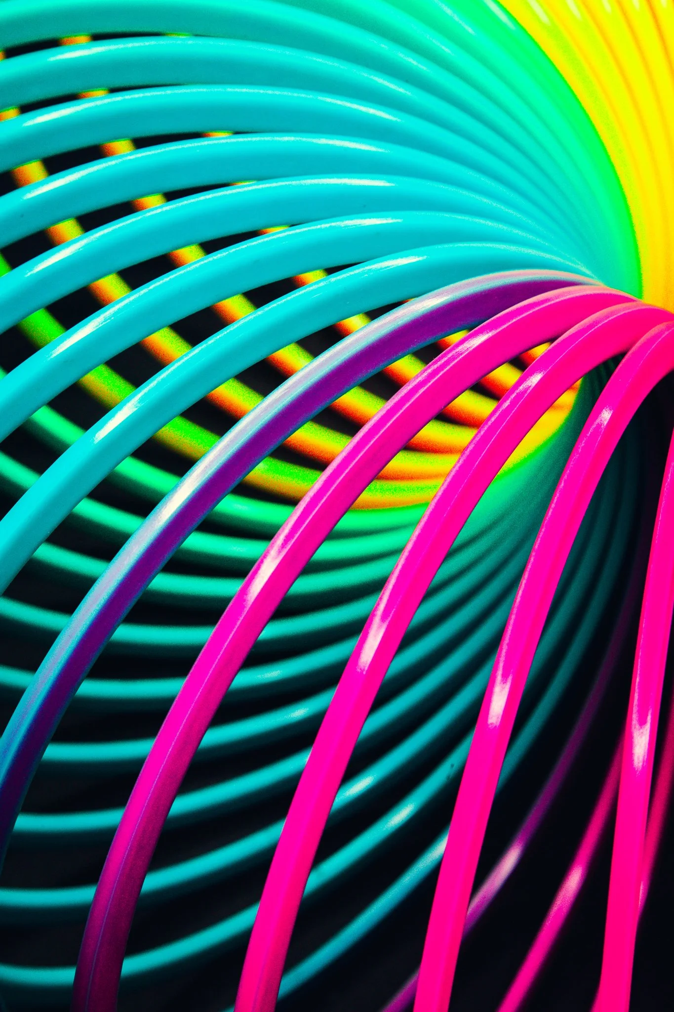 Close-up of colorful plastic spiral coils in pink, blue, green, yellow, and orange, on a black background.