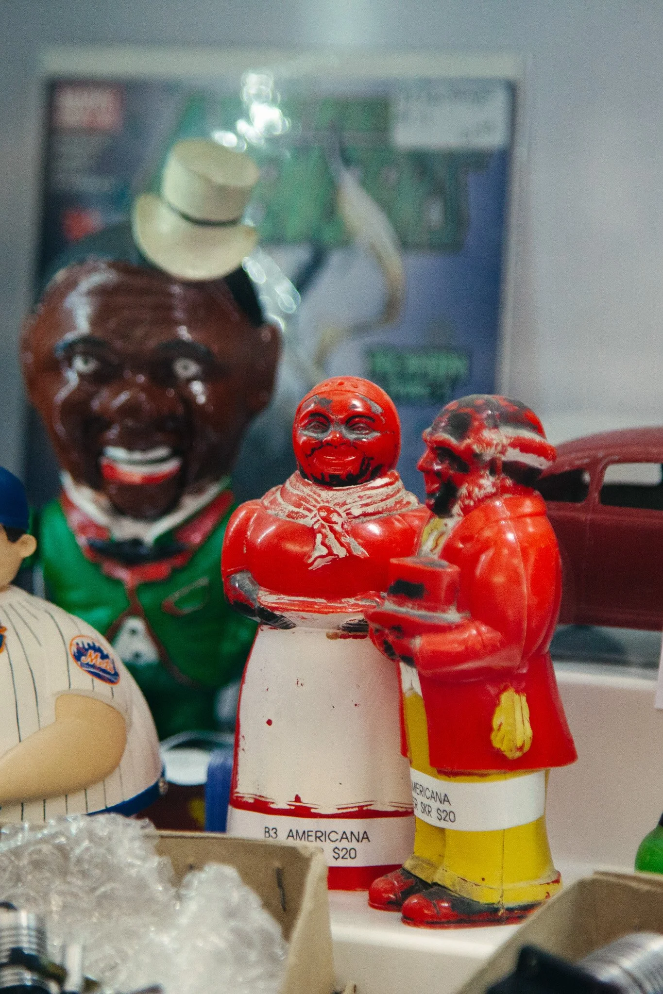 Colorful vintage figurines on display, including a red figure with a smiling face and a yellow figure inside a red jacket, with other painted figures and a blurred background.