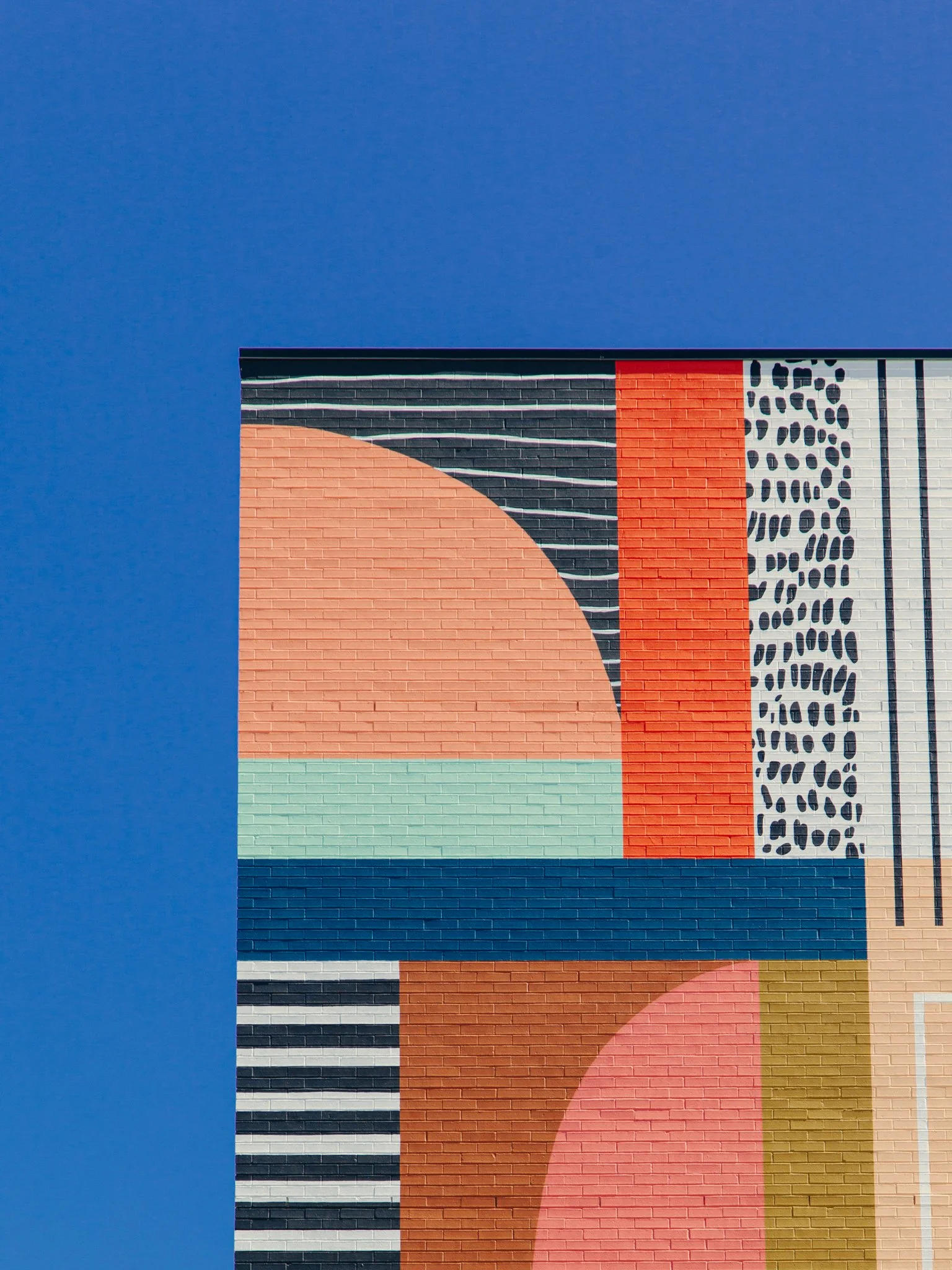 Colorful mural on a brick wall featuring geometric shapes and patterns, with a large blue background.