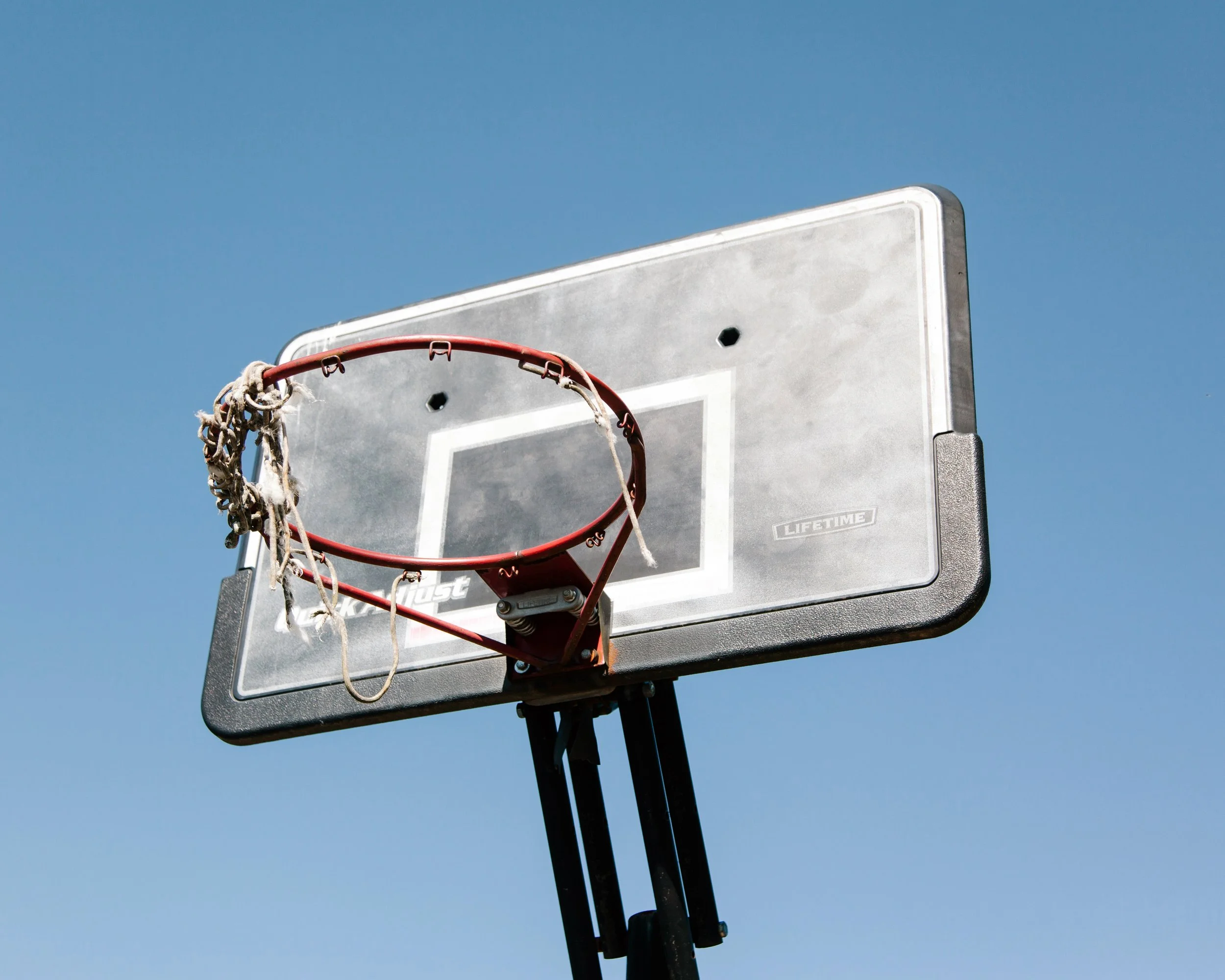 A basketball hoop and backboard mounted on a pole against a clear blue sky.