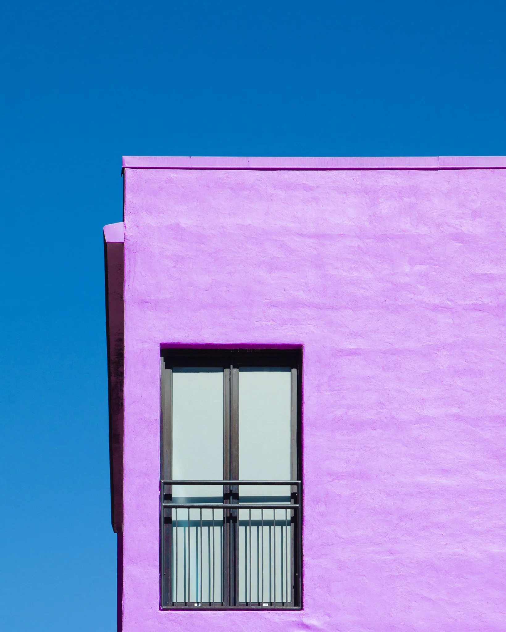 Colorful pink building with a metal barred window or balcony against a bright blue sky.
