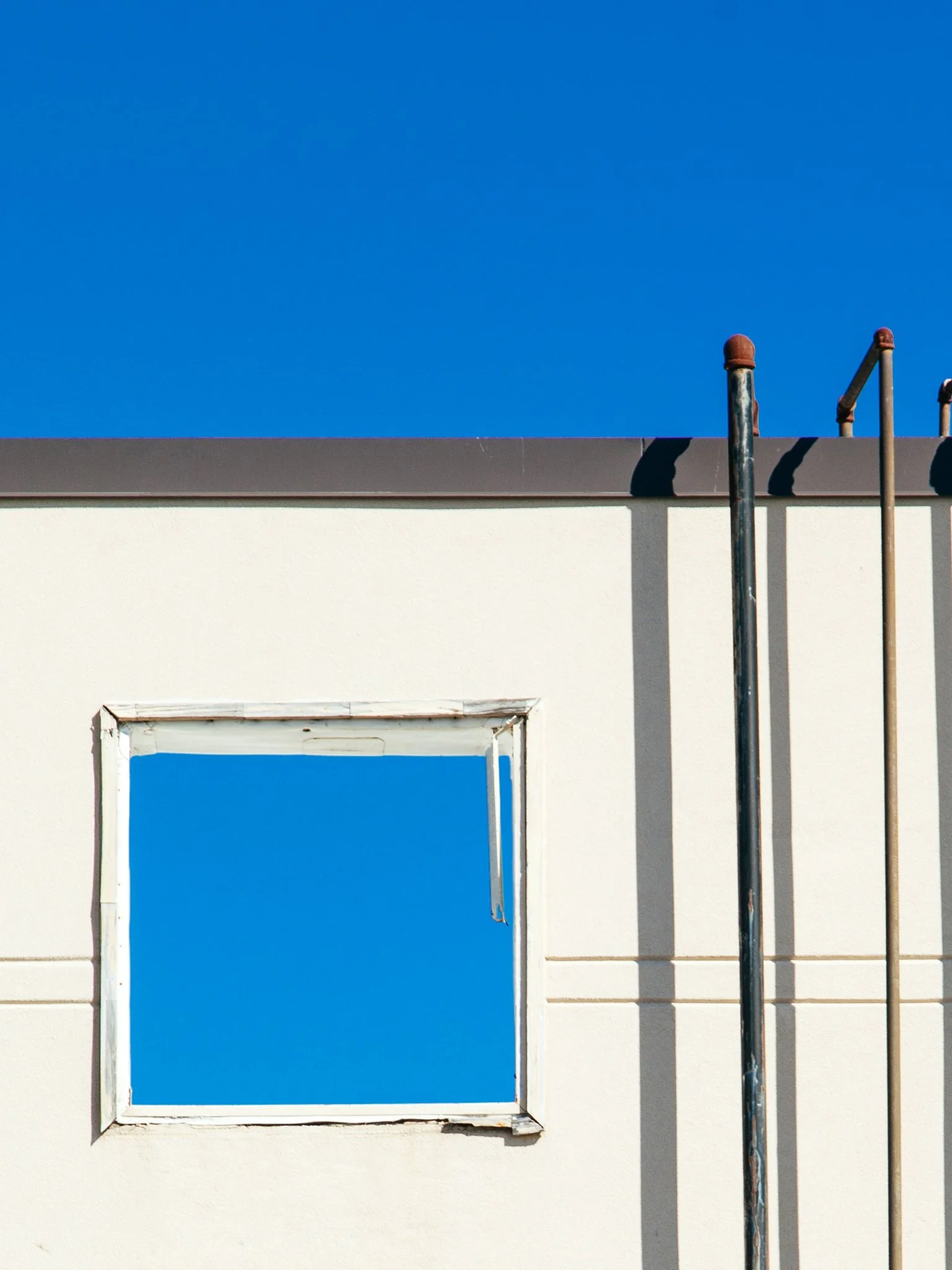 A building with a large rectangular window and three visible pipes at the top, with a clear blue sky in the background.
