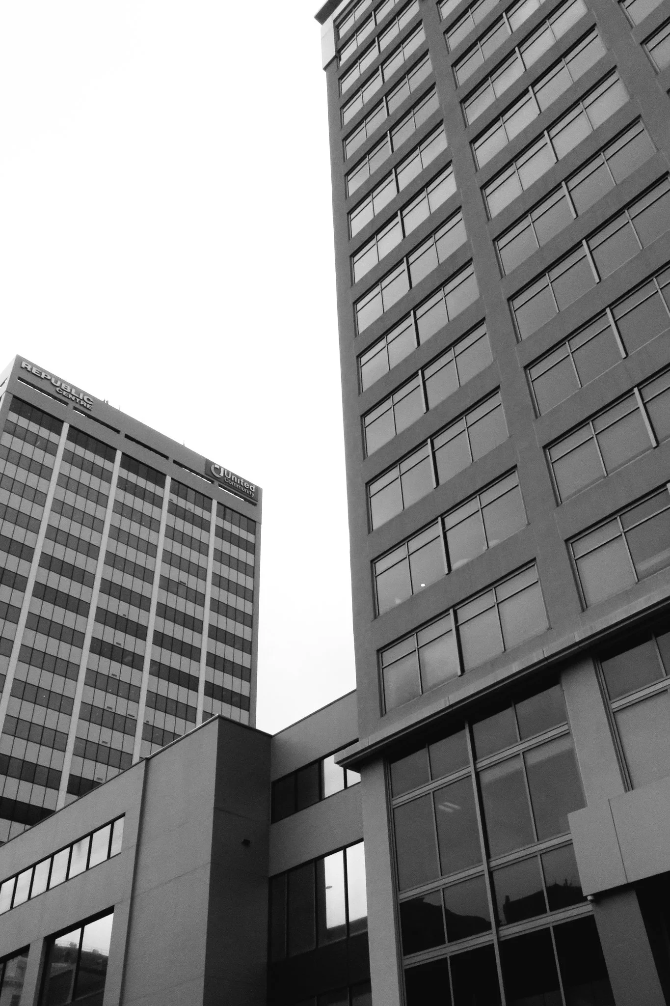 Black and white photograph of modern high-rise buildings with glass windows and geometric architectural designs.