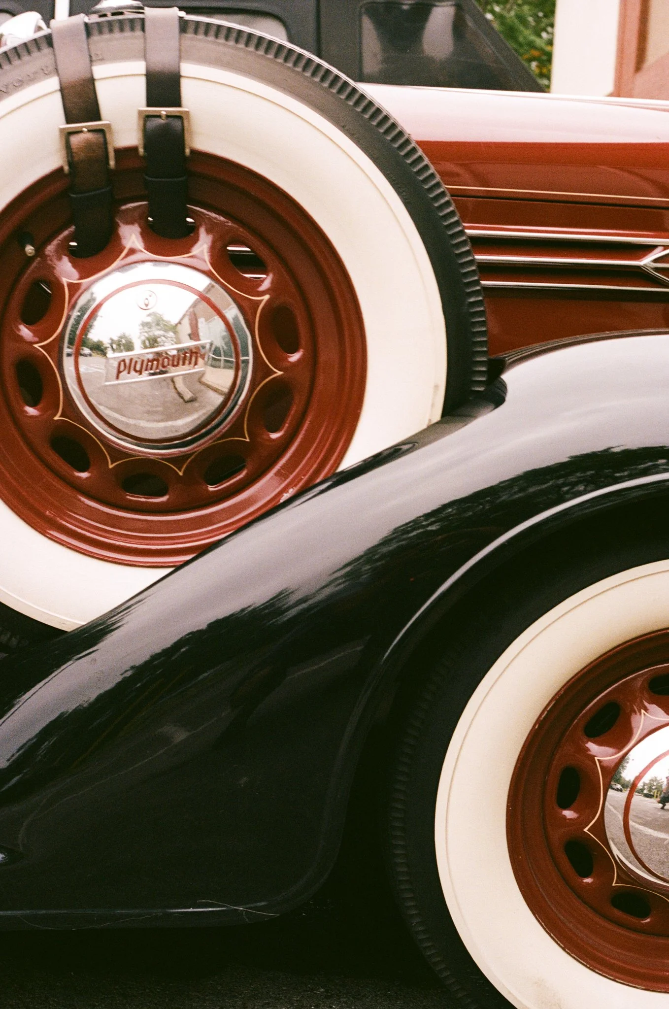 Close-up of vintage car tires with whitewall design and red rims, reflections on shiny hubcaps displaying the word 'playmouth'.