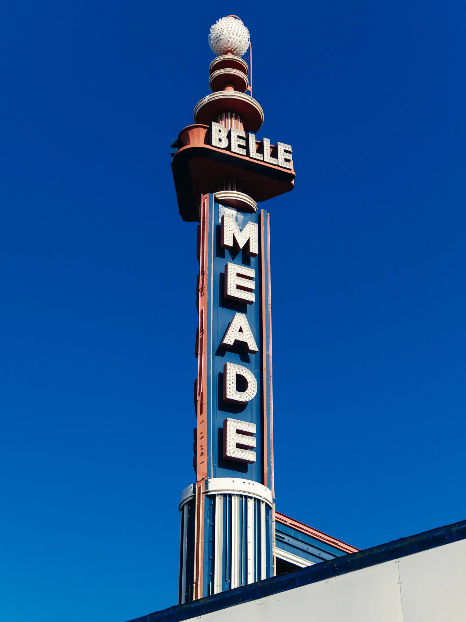 Vertical neon sign reading 'BELLE' and 'MEAD' against a clear blue sky, with part of a building or structure at the bottom.