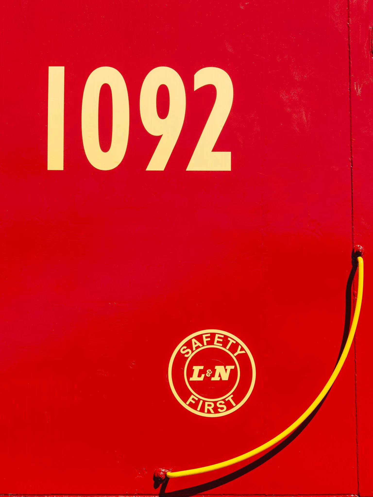 Red fire safety equipment box with the number 1092 and a safety L&N First logo sticker, yellow and black wires attached.