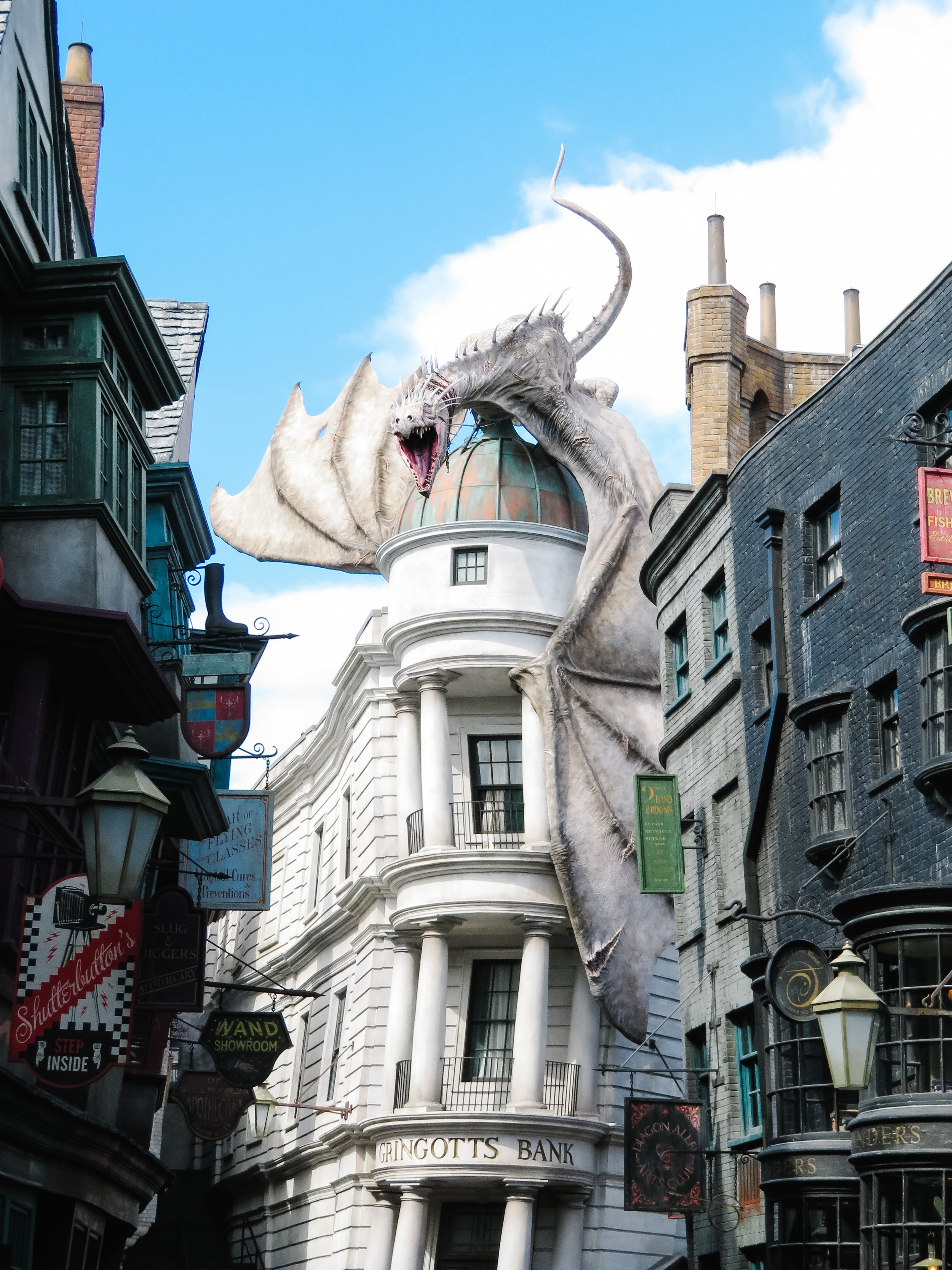 A giant dragon prop perched above buildings on a city street, with open mouth and sharp teeth, part of a Harry Potter-themed attraction.