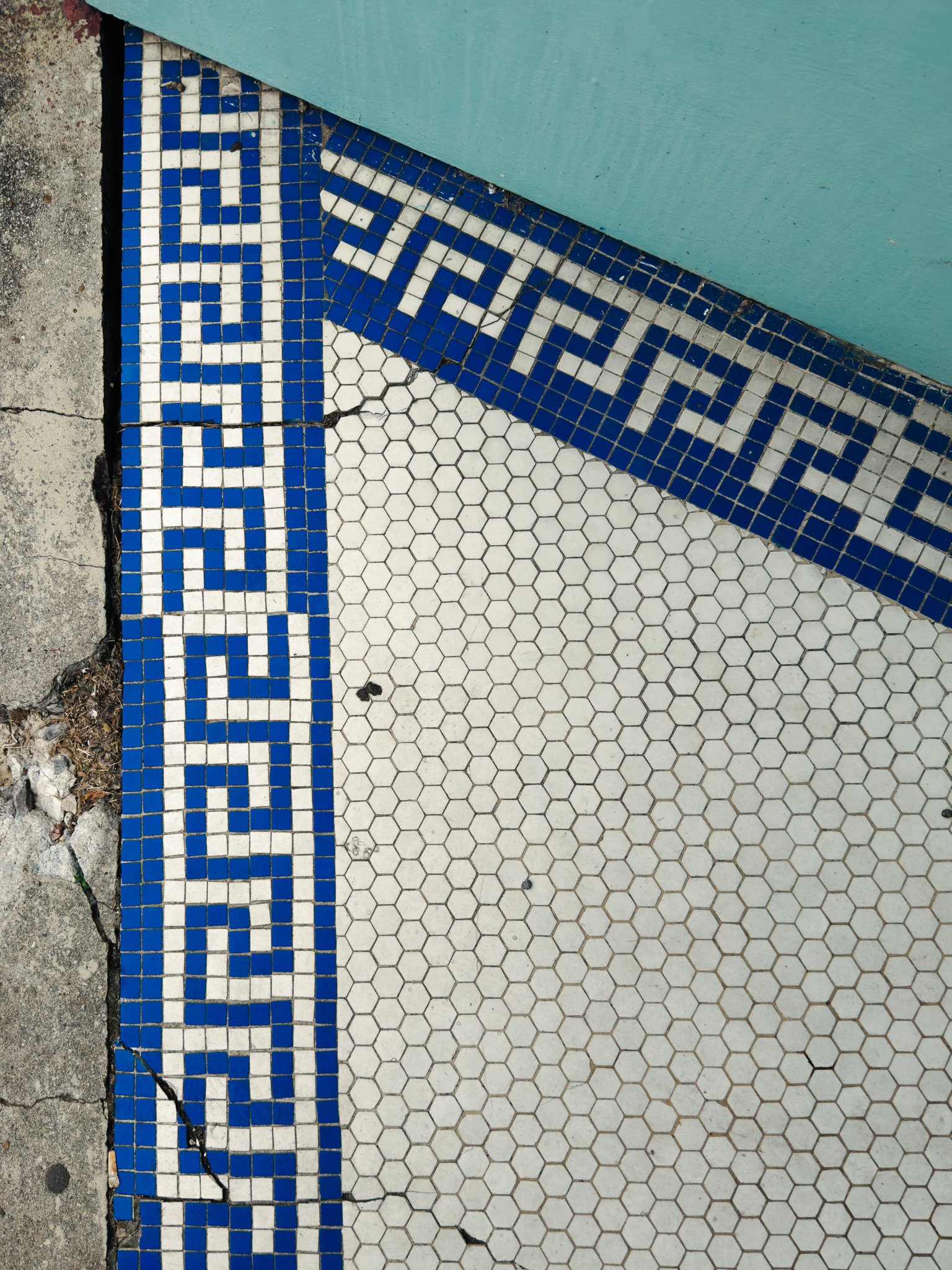 Close-up photo of tiled floor with the words 'STAY SAFE' written in blue tiles on a white background, adjacent to a light blue wall and a cracked concrete surface.