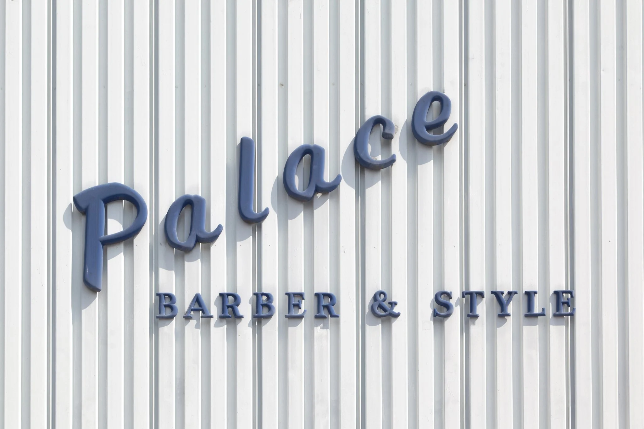 Sign on a white corrugated metal wall that reads "Palace" in large blue letters and "Barber & Style" underneath.