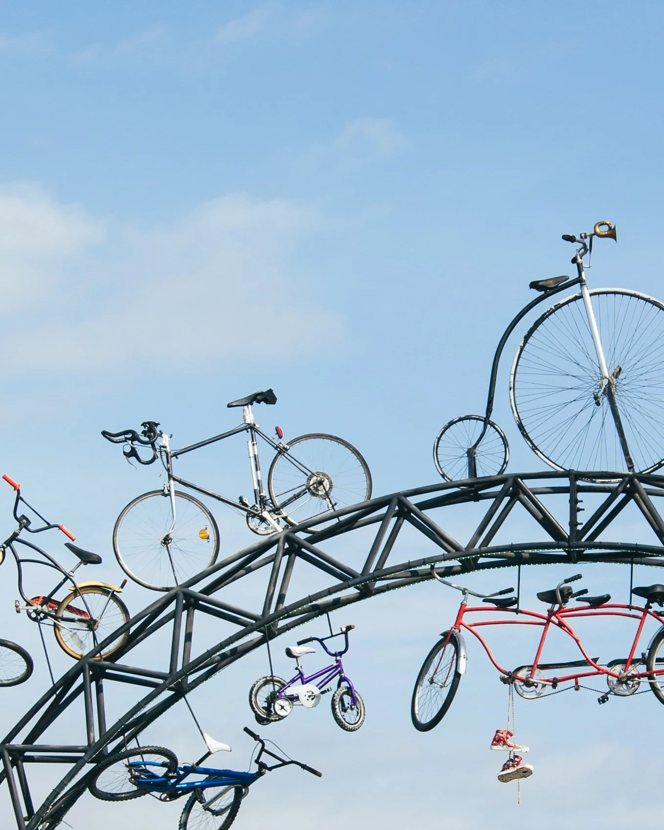 Bicycles hanging on a metal sculpture against a blue sky with clouds.