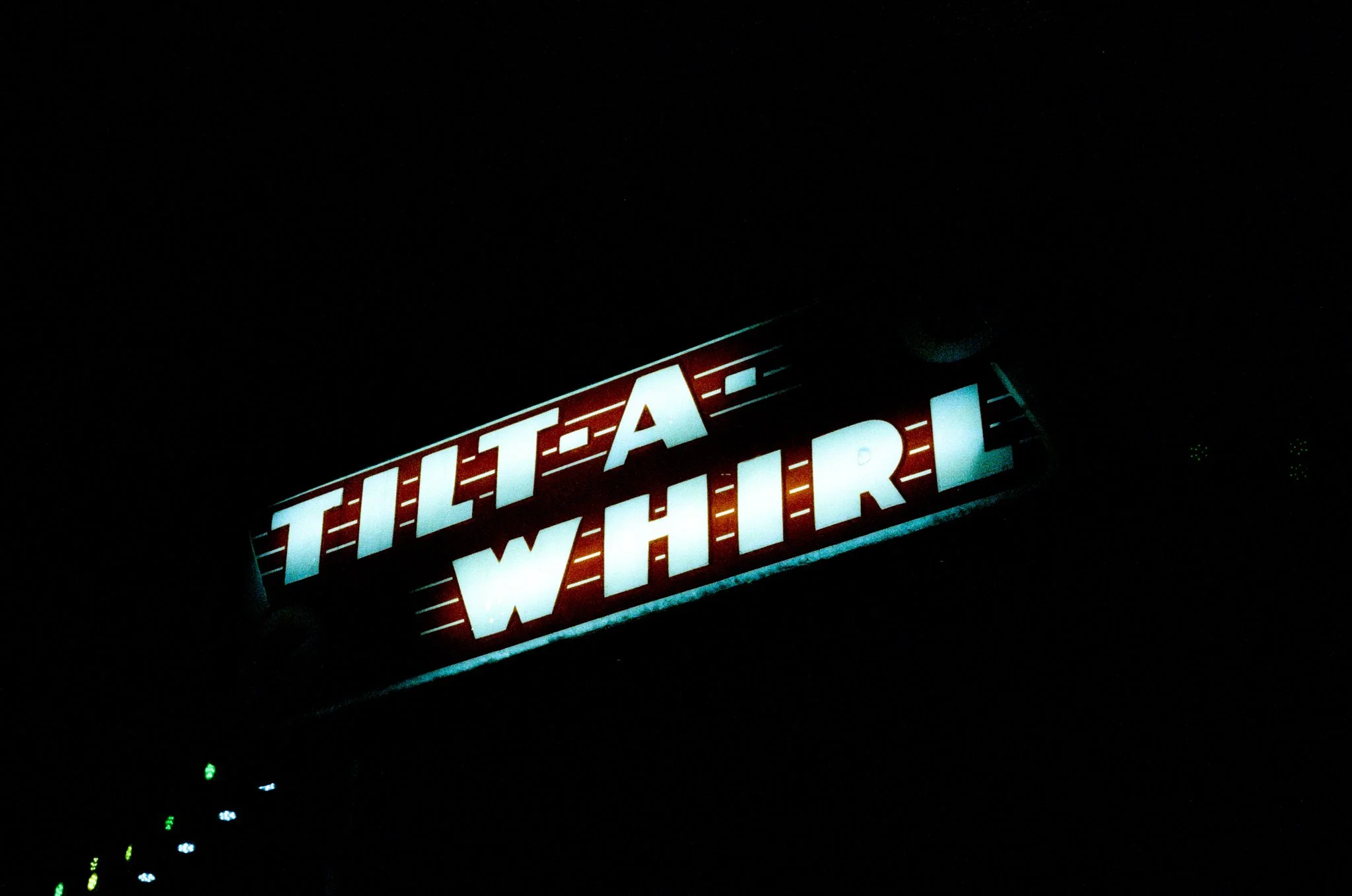 Neon sign reading 'TILT-A-WHIRL' in the dark.